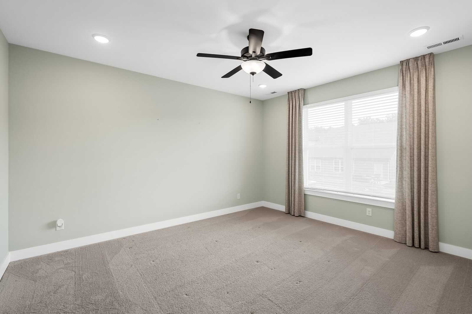 Bright secondary bedroom with ceiling fan, large curtained window, and pale green walls in Davidson Homes The Ridgeport, Gallatin, TN