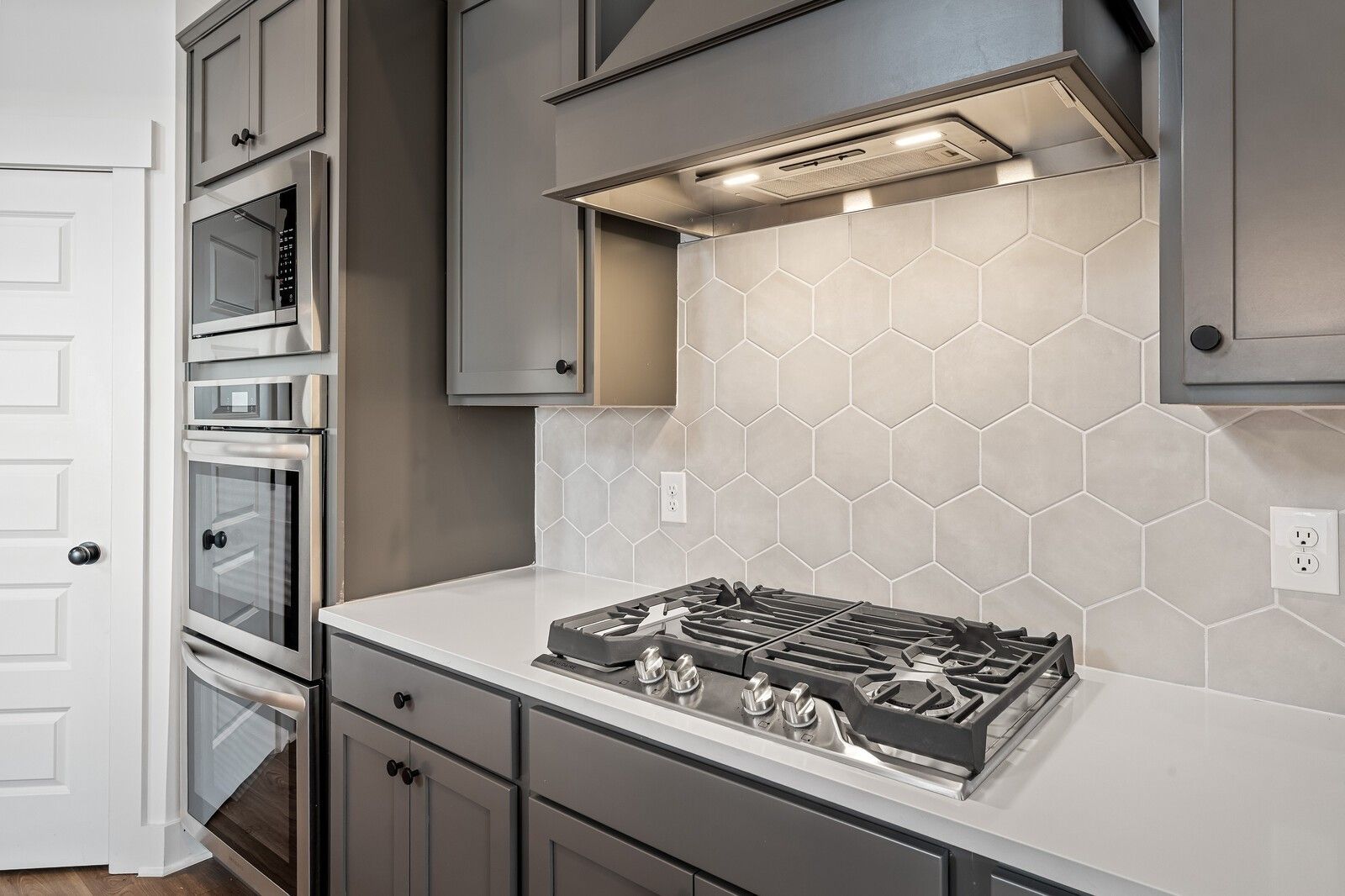 Modern gray kitchen with shaker cabinets, white quartz counters, stainless gas range, double ovens, and hexagon tile backsplash in The Ridgeport, Gallatin, TN