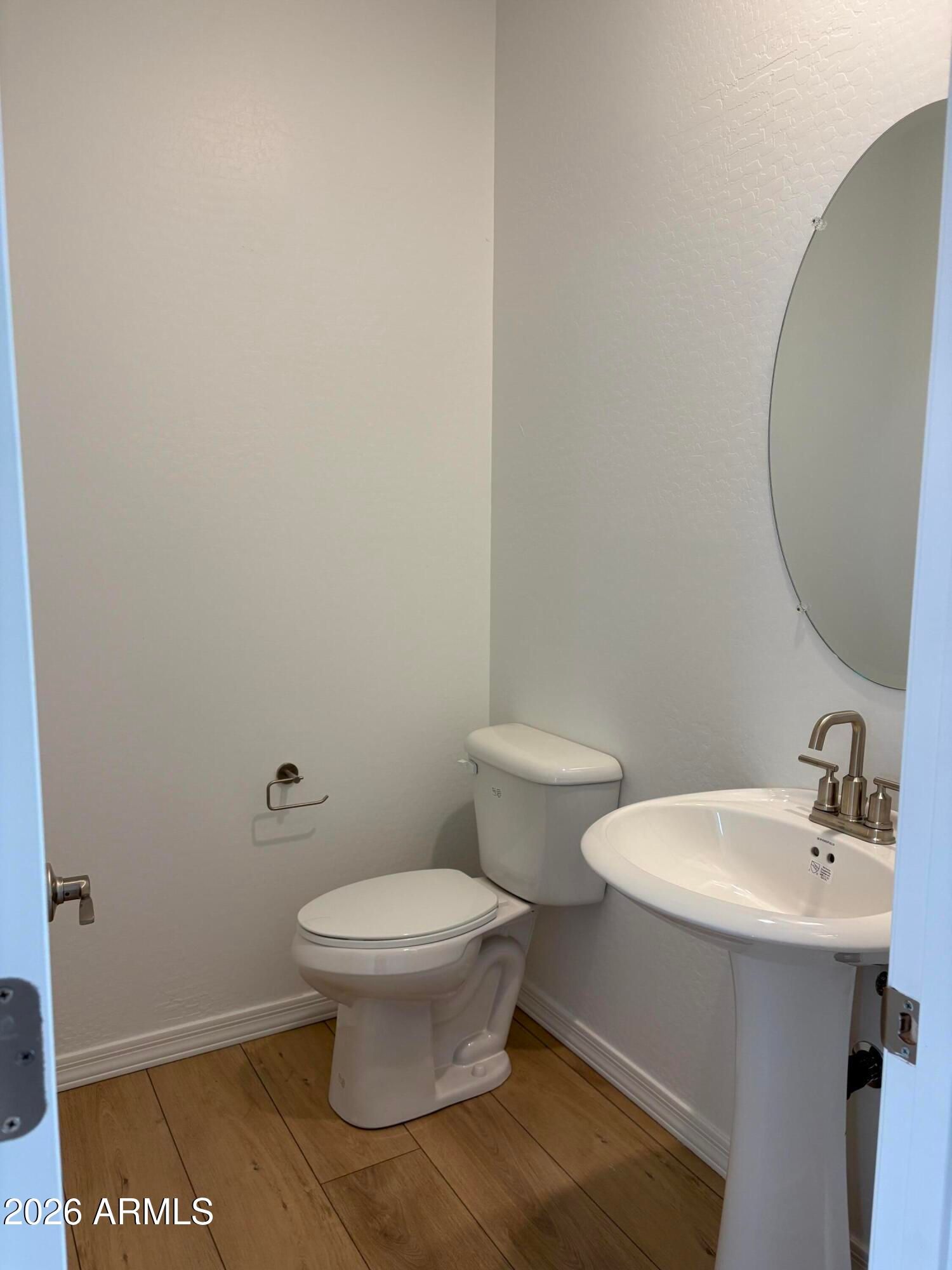Powder room with pedestal sink, oval mirror, and white toilet on wood-look flooring in Davidson Homes Evergreen B, Cottonwood, AZ