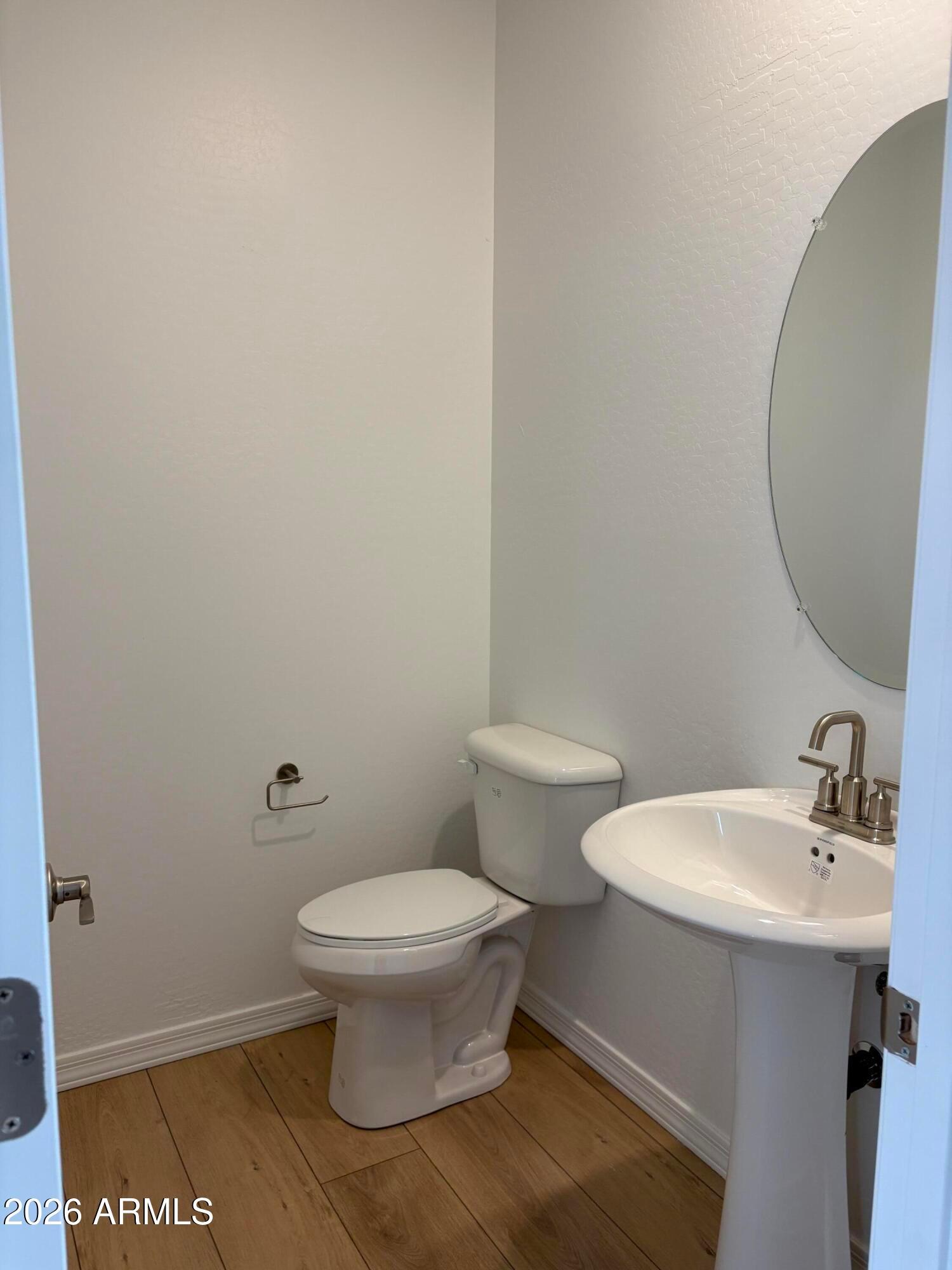 Powder room with pedestal sink, oval mirror, and white toilet on wood-look flooring in Davidson Homes Evergreen B, Cottonwood, AZ