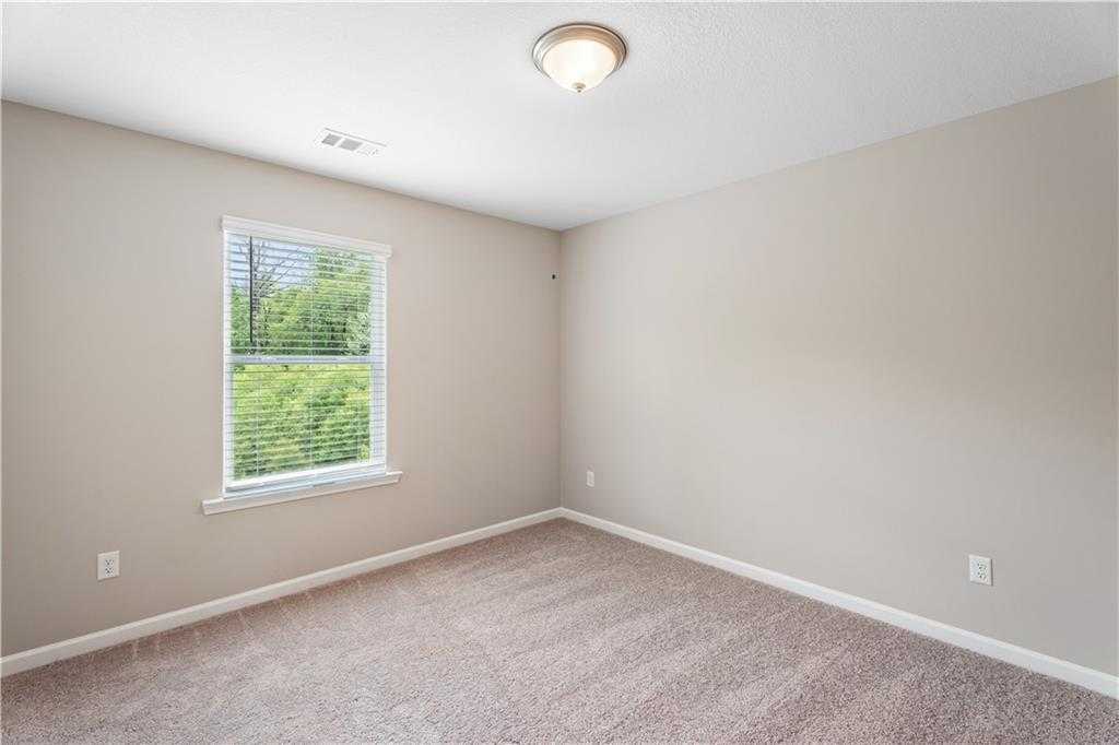 Bright empty secondary bedroom with beige walls, carpet floor, and window view of trees in Davidson Homes The Bartlett, Phenix City, Alabama