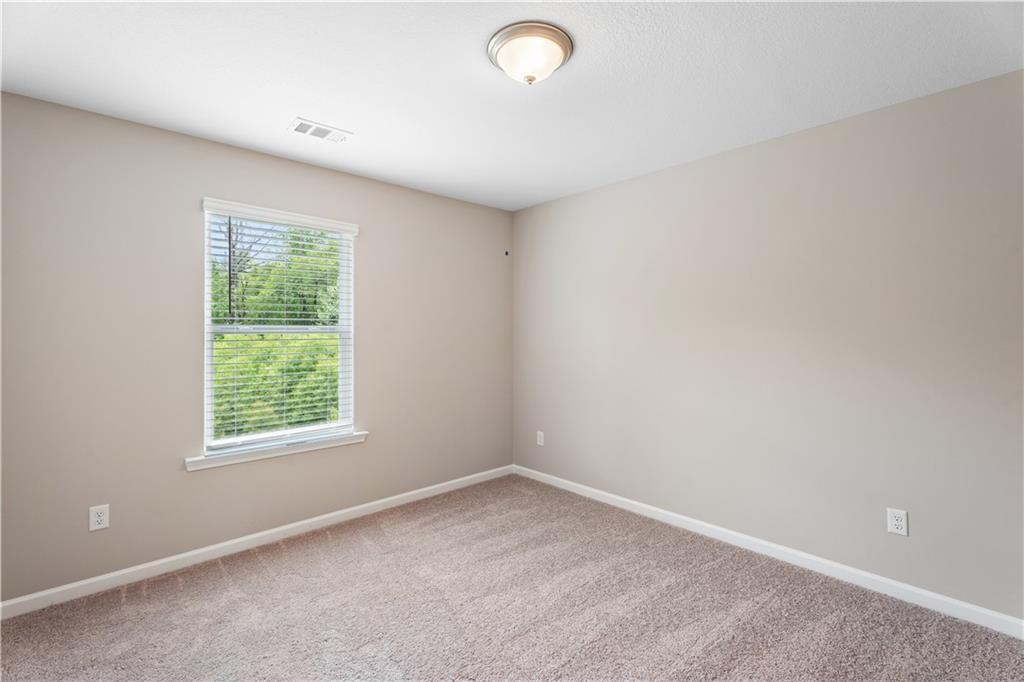 Bright empty secondary bedroom with beige walls, carpet floor, and window view of trees in Davidson Homes The Bartlett, Phenix City, Alabama