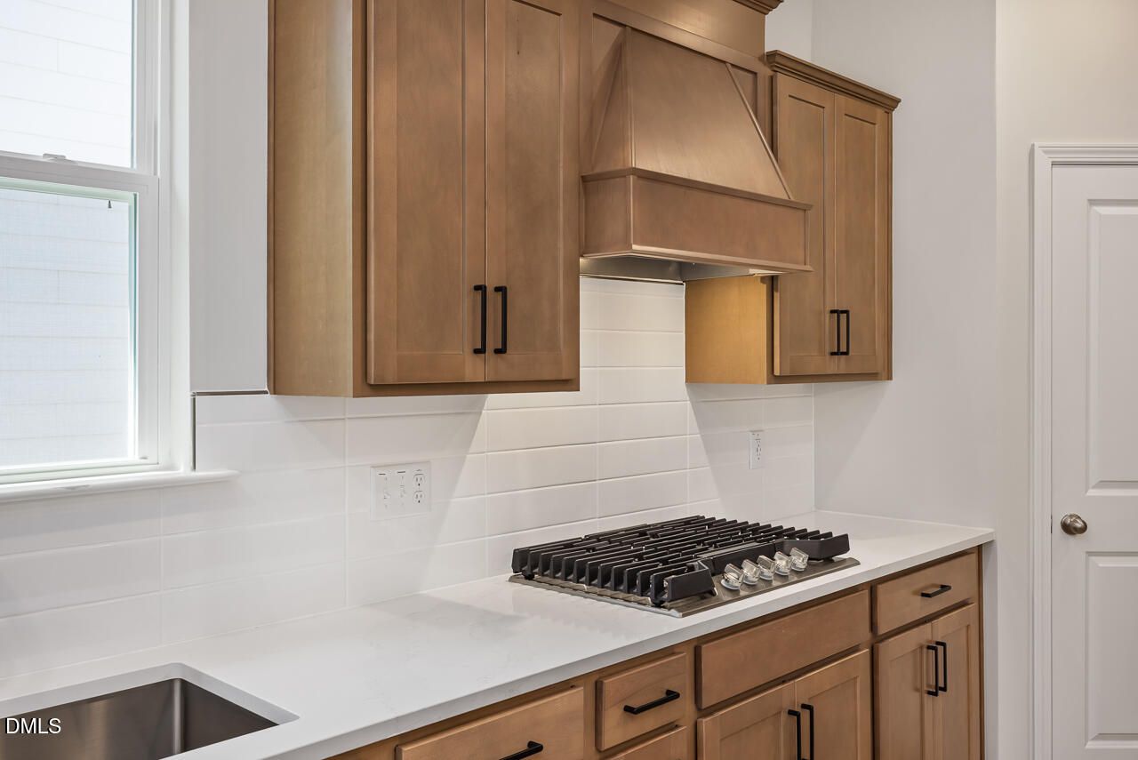 Modern kitchen with wood cabinets, gas cooktop, and white subway tile backsplash in The Ashport L at Sage on North Main.