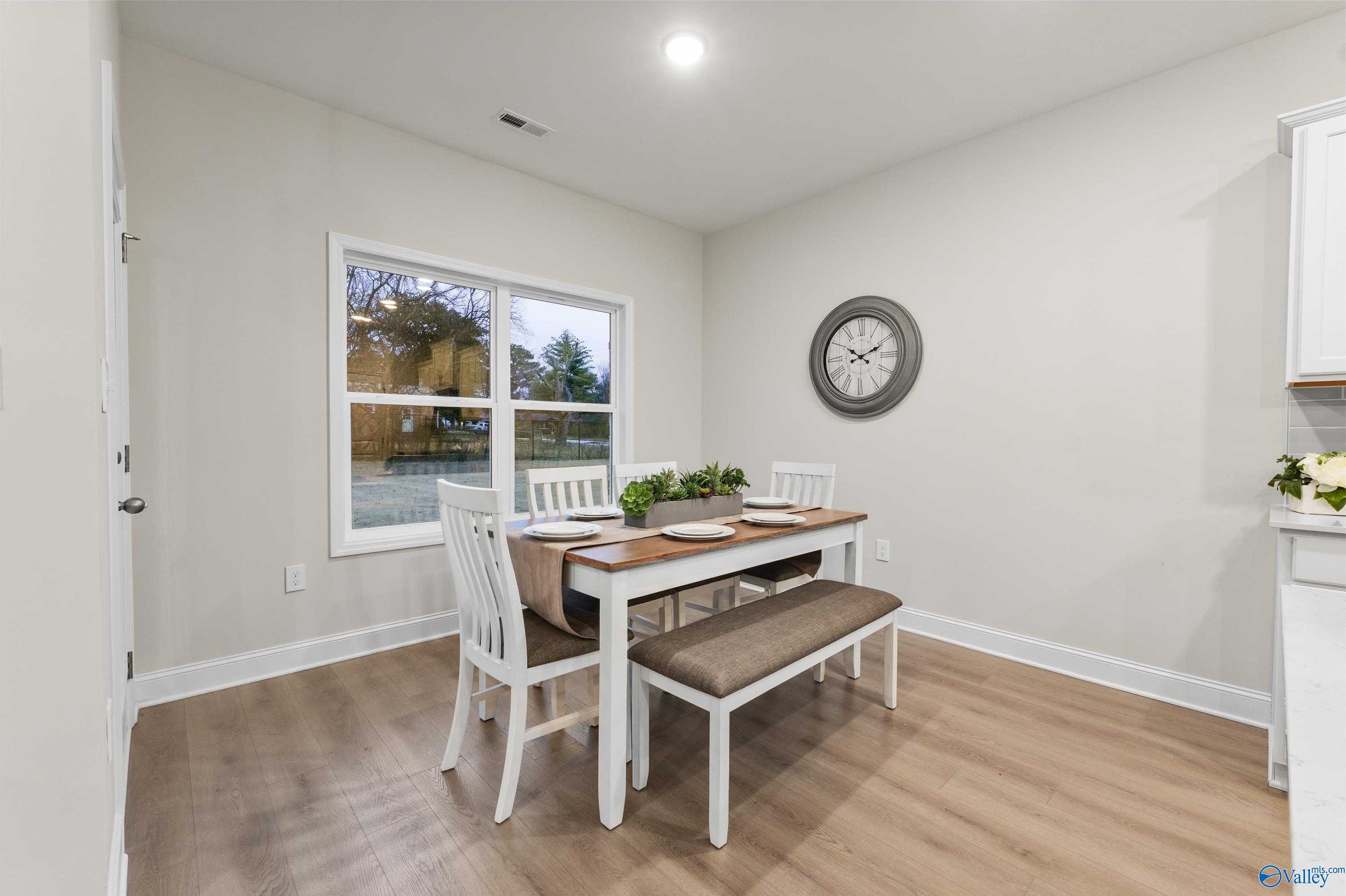 Bright dining room with wooden table, white chairs, beige bench, and floral centerpiece in The Asheville C home, Huntsville, Alabama