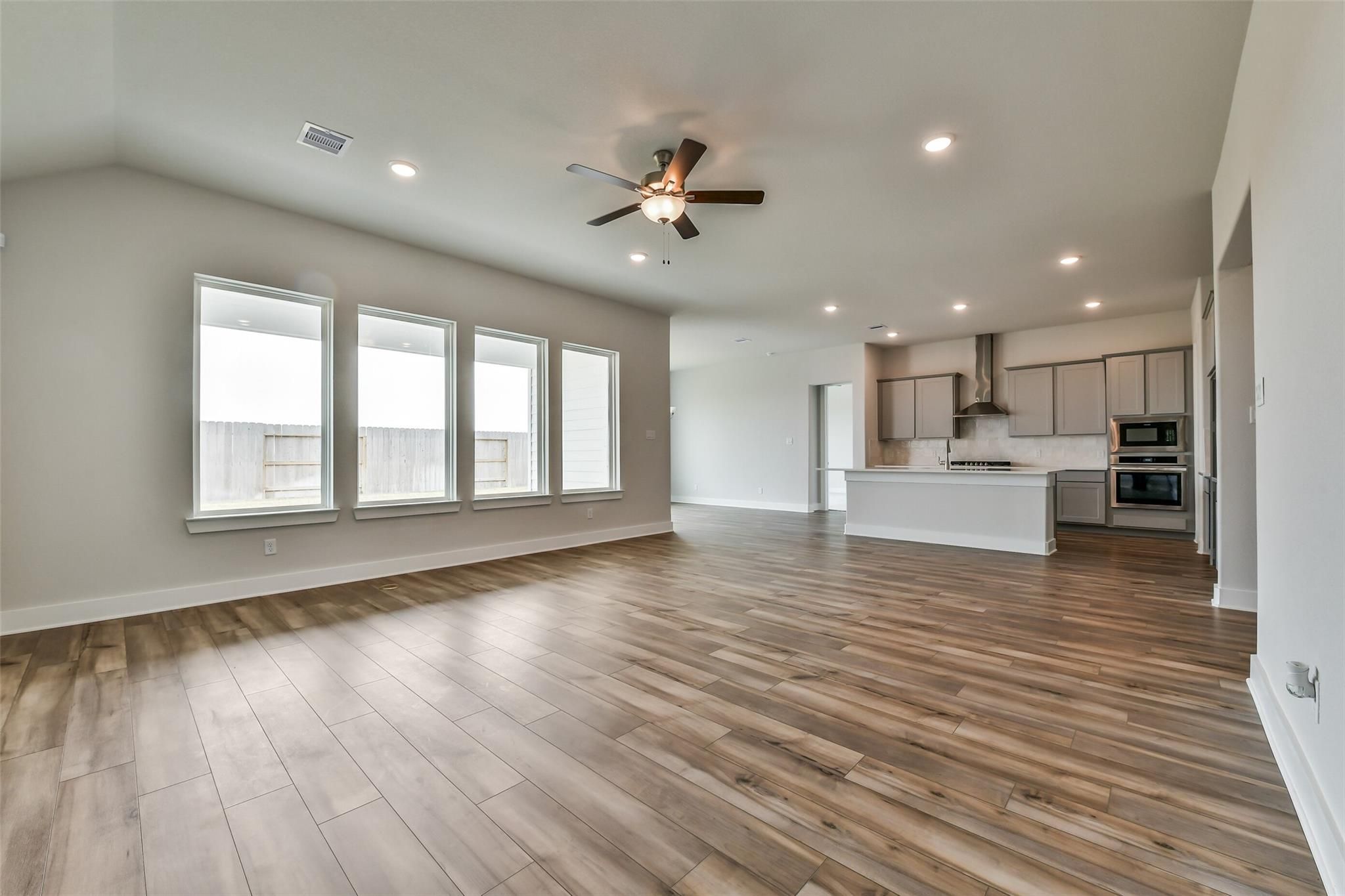 Bright open-concept living-kitchen with hardwood floors, white cabinets, island, ceiling fans, and large windows in Davidson Homes The George A