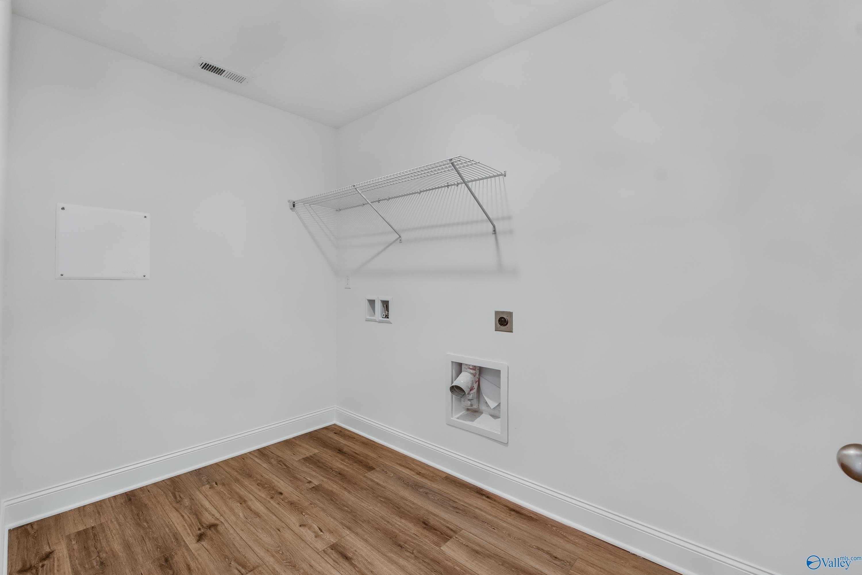 Spacious laundry room with wire shelving, washer/dryer hookups, and luxury vinyl plank flooring in Davidson Homes The Shelby A, Arab, Alabama