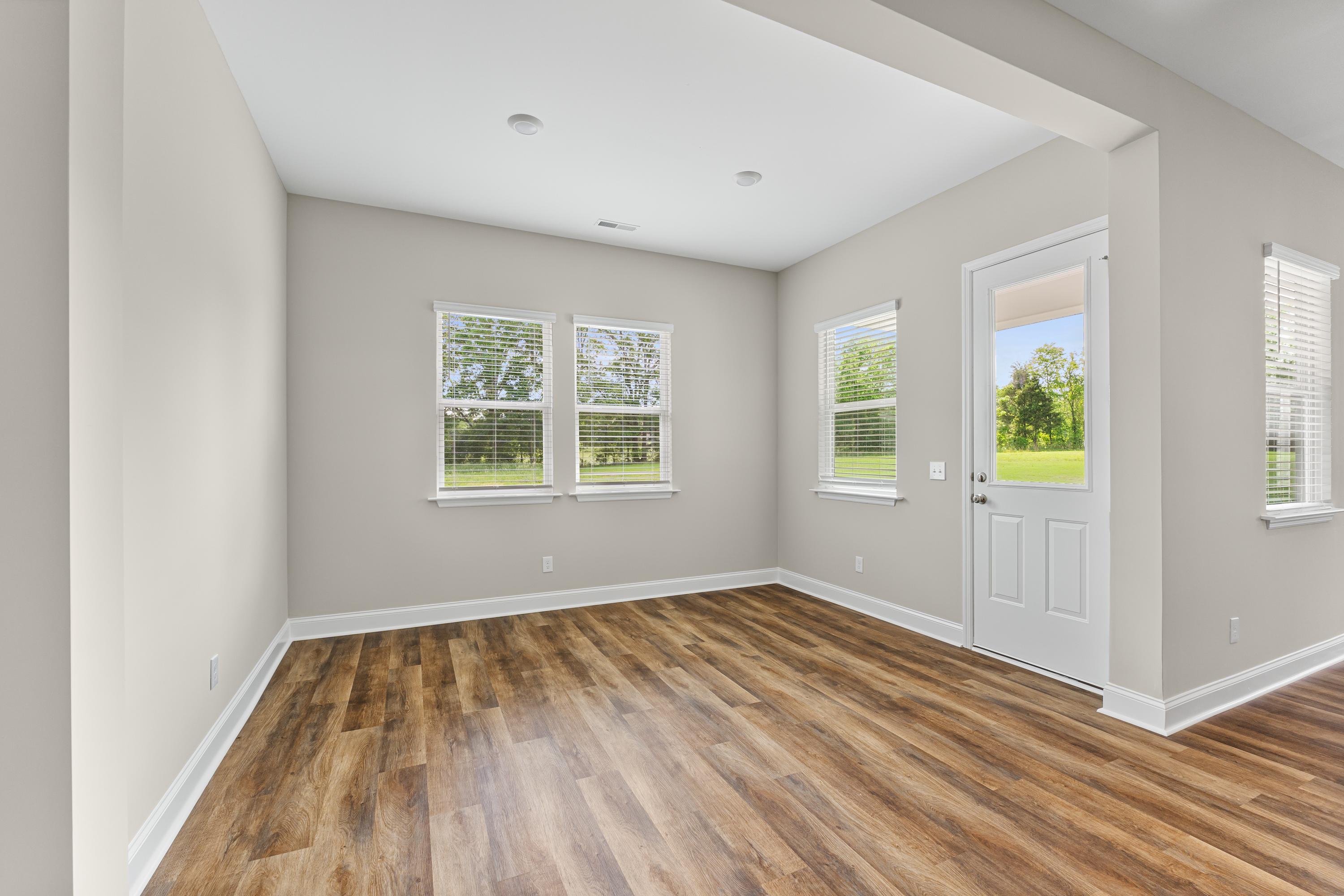Sunlit flex room in The Arcadia B by Evermore Homes, with beige walls, hardwood floors, large windows, and glass door to greenery