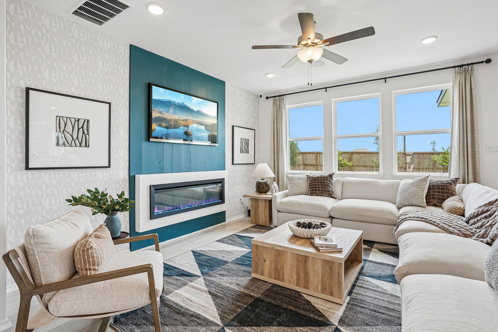 Modern living room at Morgan Meadows in San Antonio, Texas featuring a blue accent wall, electric fireplace, and sectional.