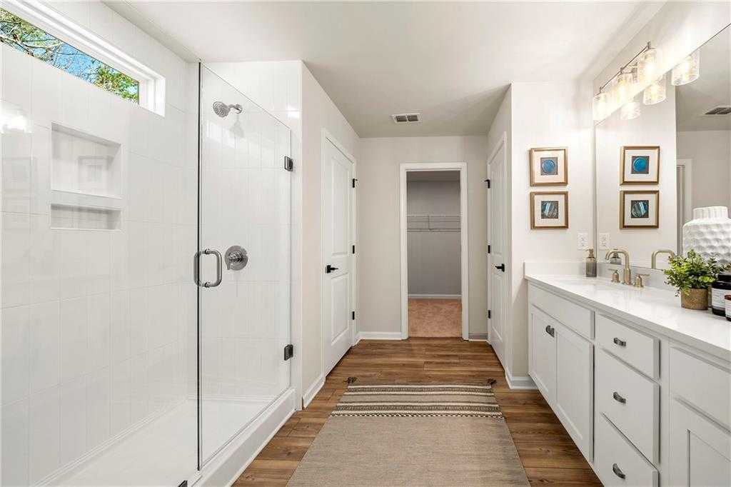 Spacious master bathroom featuring glass walk-in shower, double white vanity, and adjacent closet in Davidson Homes The Hickory B, Riverwood, Dallas, GA