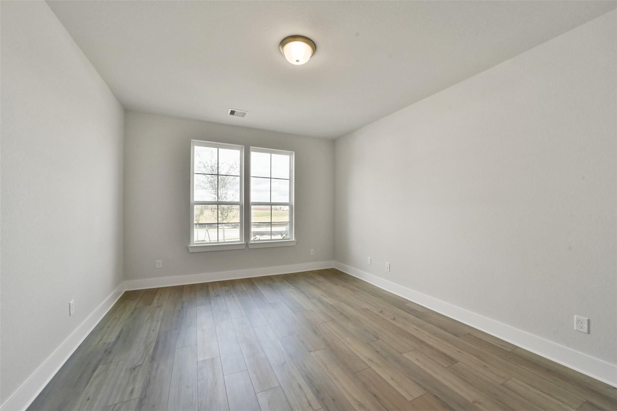 Bright empty bedroom with large windows and light wood floors in Davidson Homes The Zion A, Lago Mar, Texas City