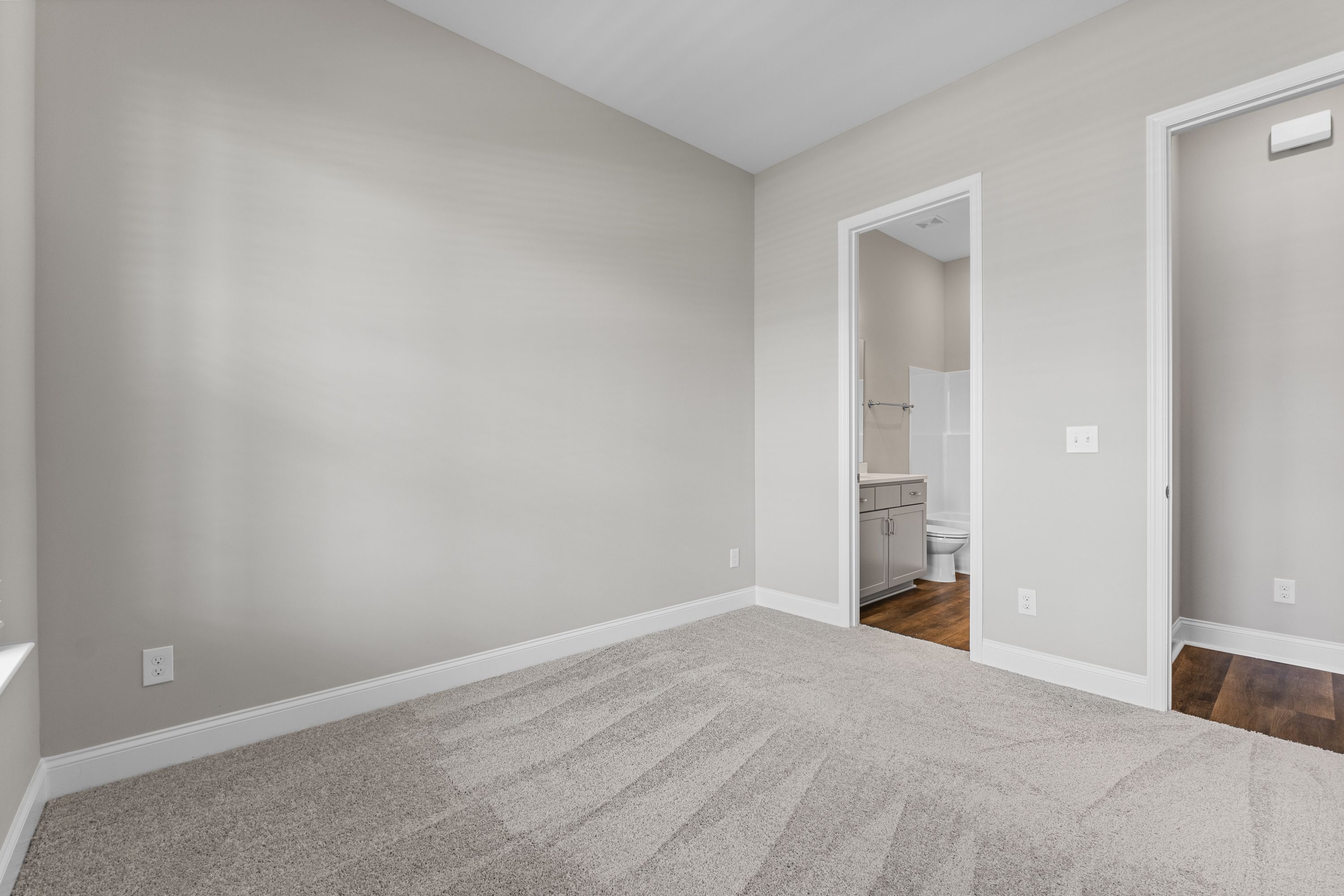 Spacious master bedroom in The Arcadia E with gray walls, carpeted floor, and en-suite bath featuring vanity and toilet