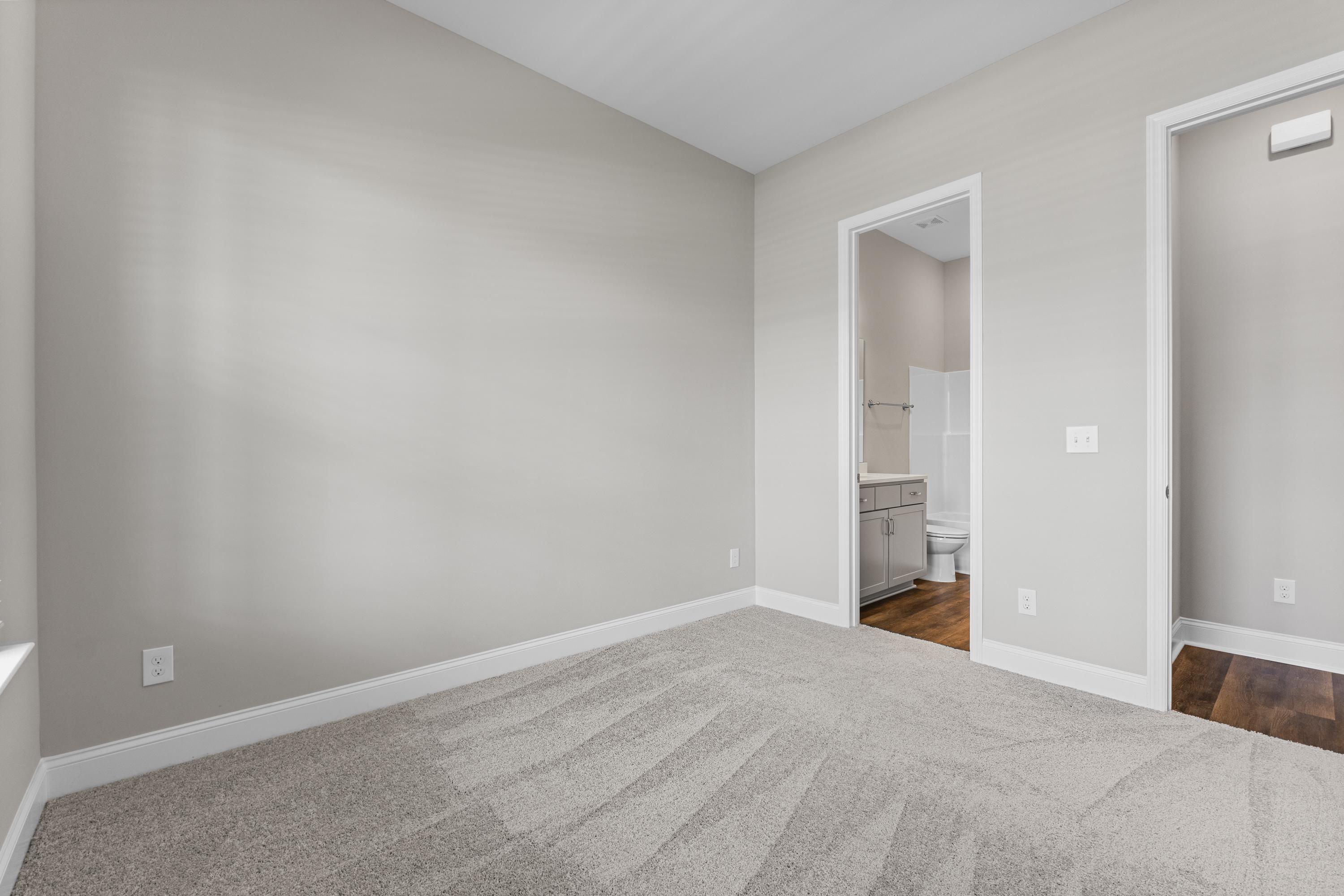 Spacious secondary bedroom in The Arcadia B with attached bath, gray carpet floors, and neutral walls