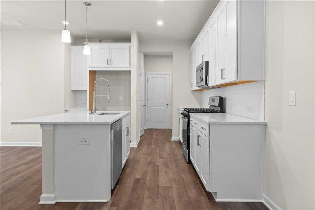 Modern white kitchen with large island, stainless steel appliances, and hardwood floors in The Marion B, Kennesaw, Georgia