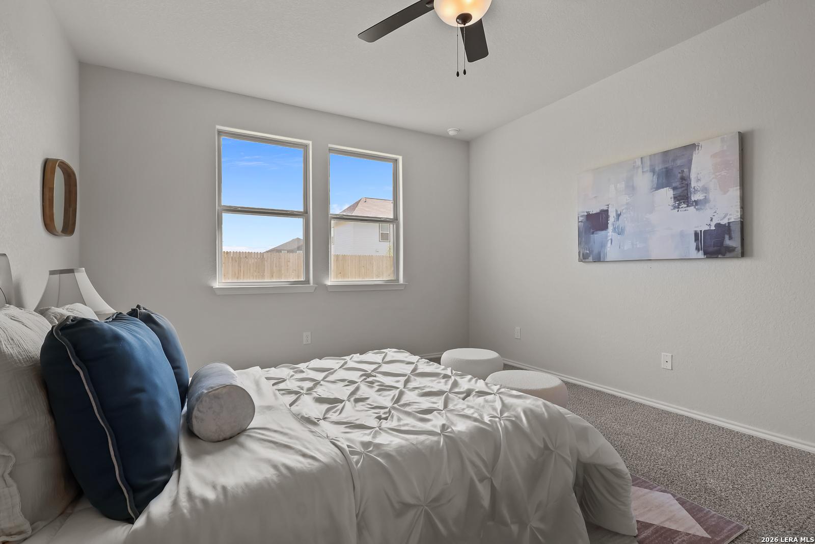 Cozy secondary bedroom with ceiling fan, dual windows, abstract wall art, tufted bed in The Daphne H by Davidson Homes, Seguin Texas
