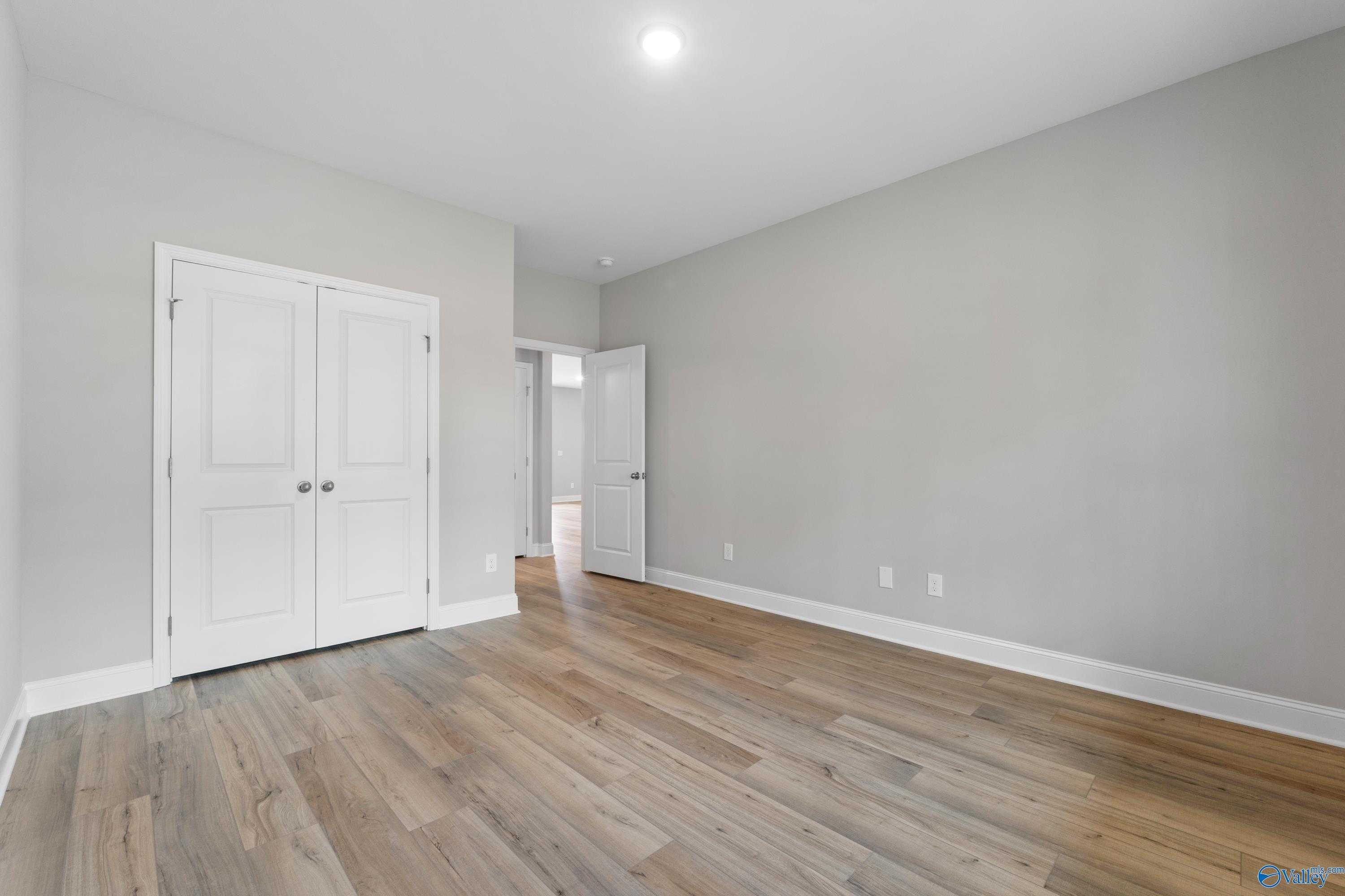 Spacious bedroom with gray walls, hardwood floors, white bi-fold closet doors in Davidson Homes Chelsea B, New Market, Alabama