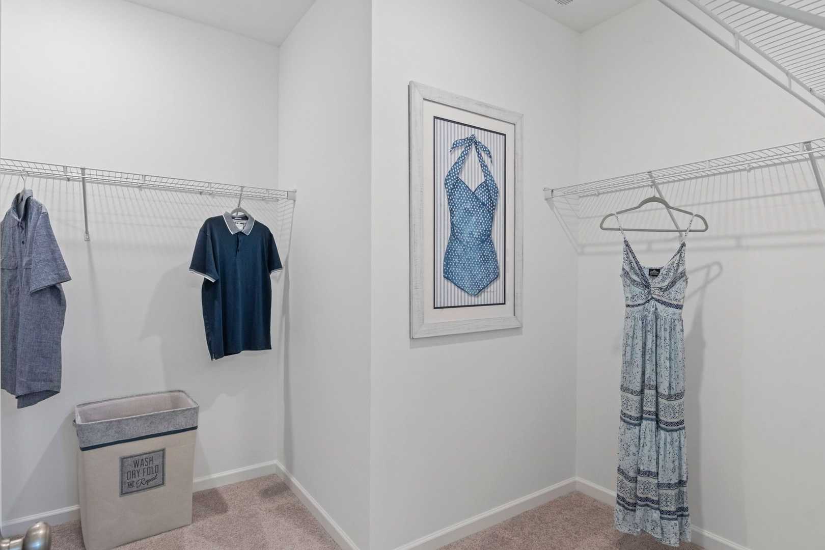 Spacious walk-in closet in The Phoenix master suite featuring wire shelving, hanging apparel, and framed blue dress artwork