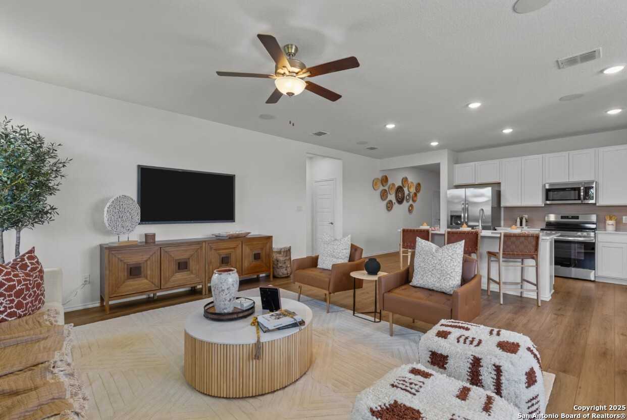 Modern open-concept living room with mounted TV, leather sofa, and white kitchen in Davidson Homes The Daphne J, Elmendorf, Texas