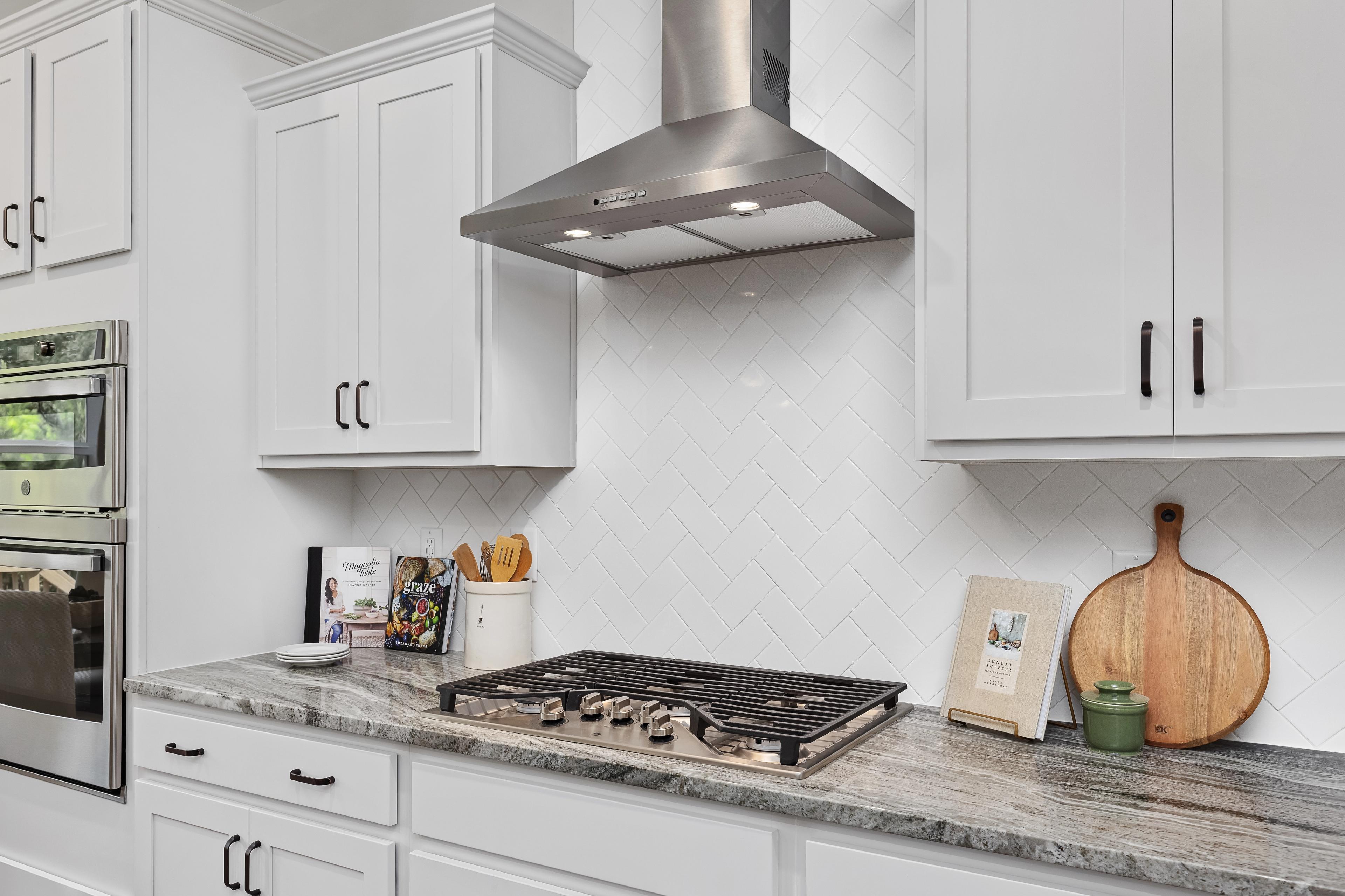 Modern kitchen in Woodland Crossing, Zebulon NC with white shaker cabinets, gas cooktop, stainless hood, subway tile backsplash, granite counters by Davidson Homes