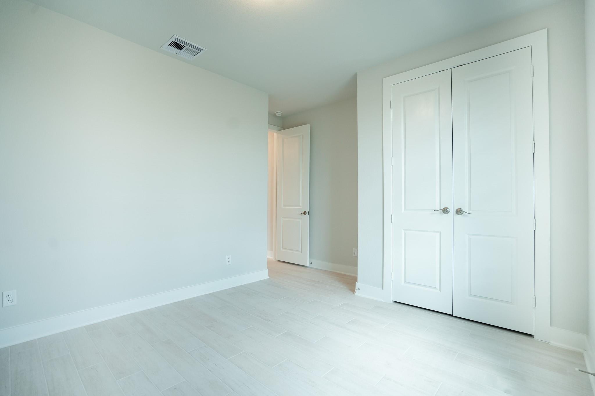 Bright secondary bedroom with white double-door closet and open bath door in Davidson Homes The Edward C, Lago Mar, Texas City