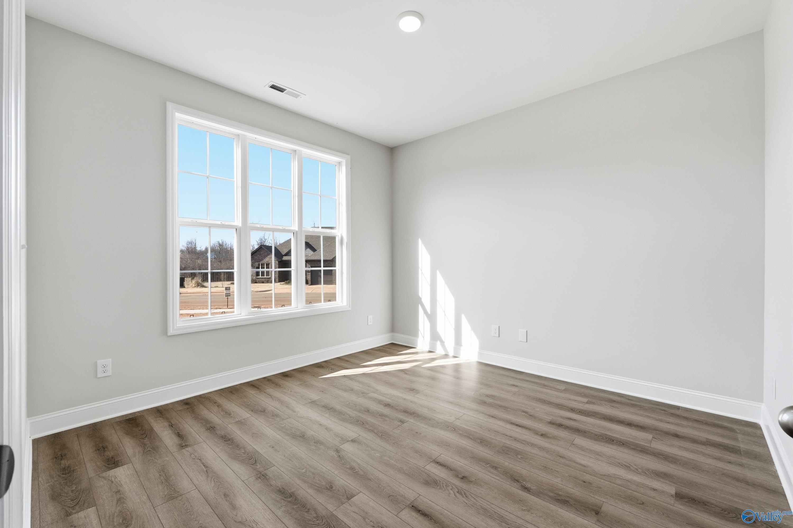 Bright empty bedroom with large sunny windows, gray walls, and luxury vinyl plank floors in Davidson Homes The Finleigh, Harvest, AL