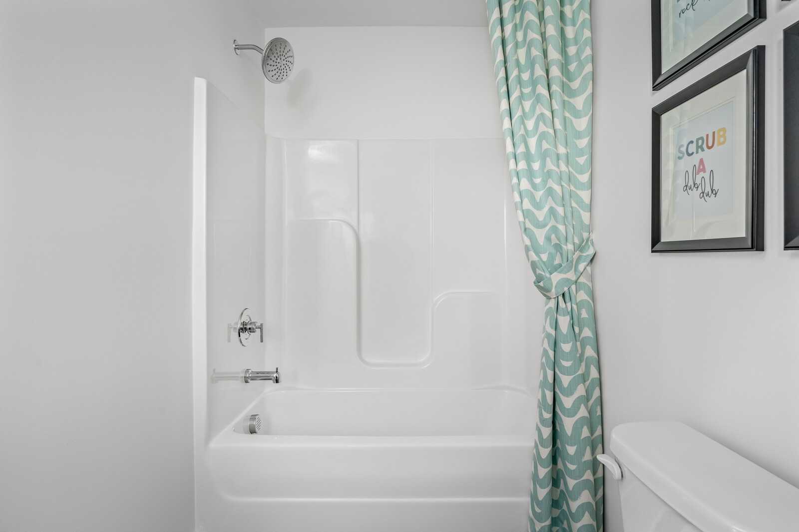 Bright bathroom with white tub-shower combo, teal curtain, and scrub art in Davidson Homes Cumberland A, Gallatin, TN