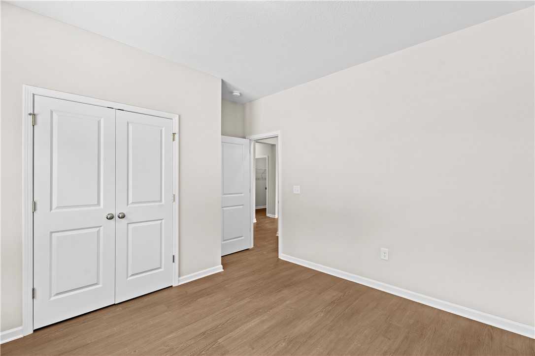 Spacious bedroom with white double closet doors, open doorway, hardwood floors, and neutral walls in Evermore Homes The Orion, Cusseta, Alabama