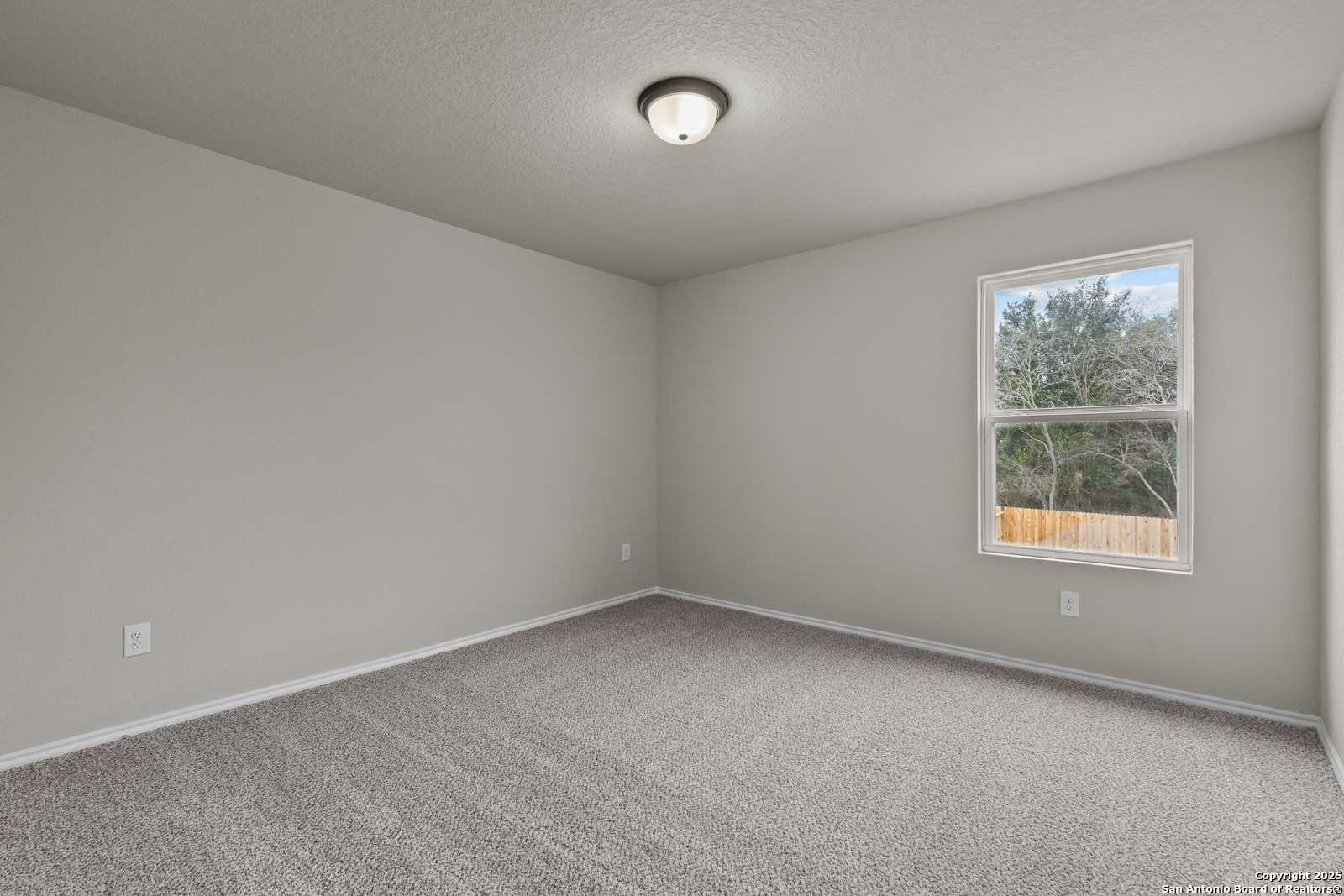Empty bedroom with light gray walls, berber carpet, ceiling light, and window view of trees in Davidson Homes The Murray I, San Antonio, Texas