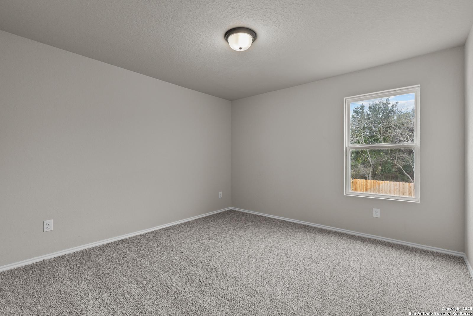 Empty bedroom with light gray walls, berber carpet, ceiling light, and window view of trees in Davidson Homes The Murray I, San Antonio, Texas