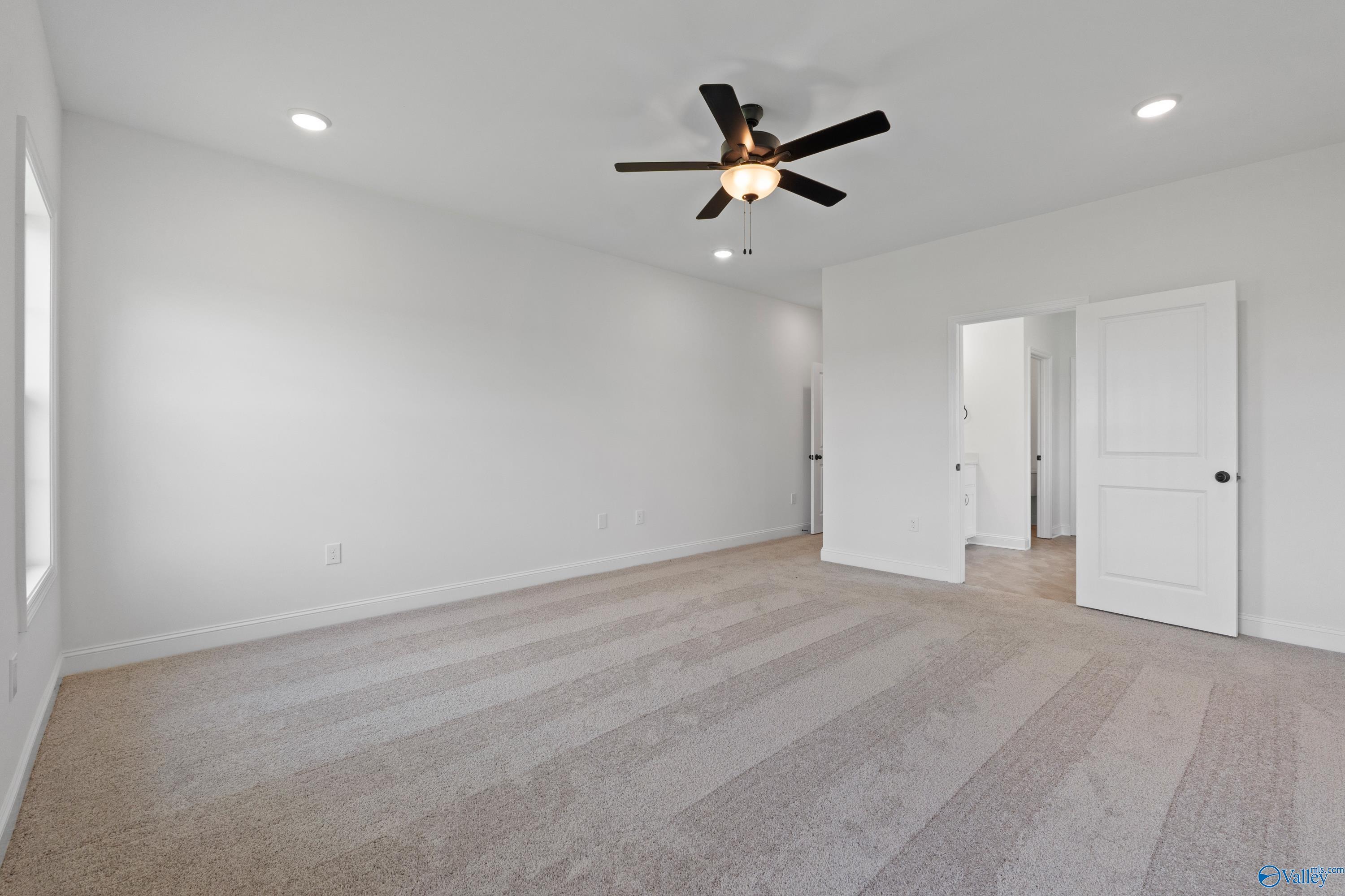 Spacious empty bedroom with beige carpet, white walls, black ceiling fan, and adjacent bath door in Davidson Homes The Rockford B, Toney, AL