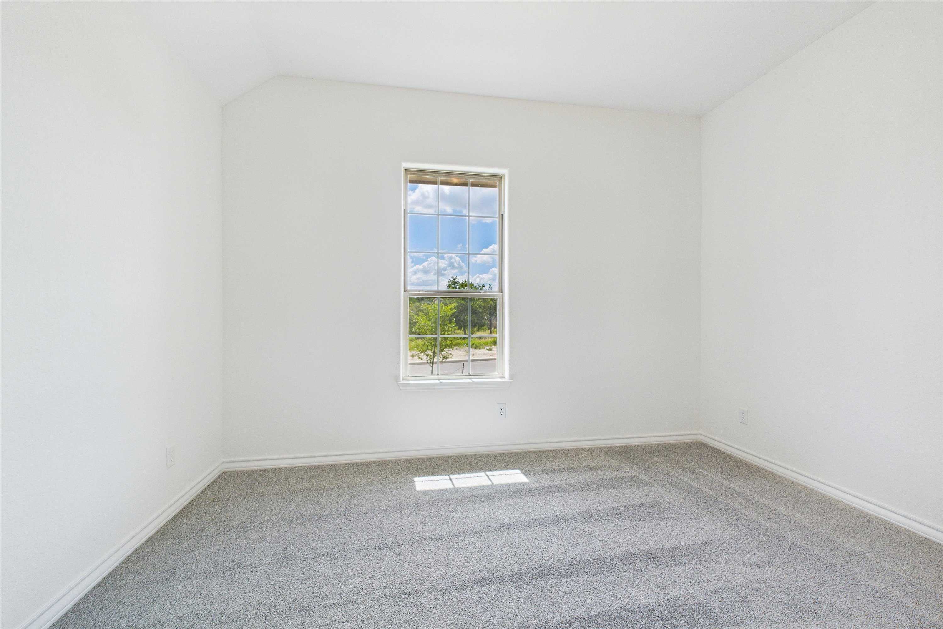 Bright empty bedroom with large window overlooking trees in Davidson Homes The Summerlin C, Castroville, Texas