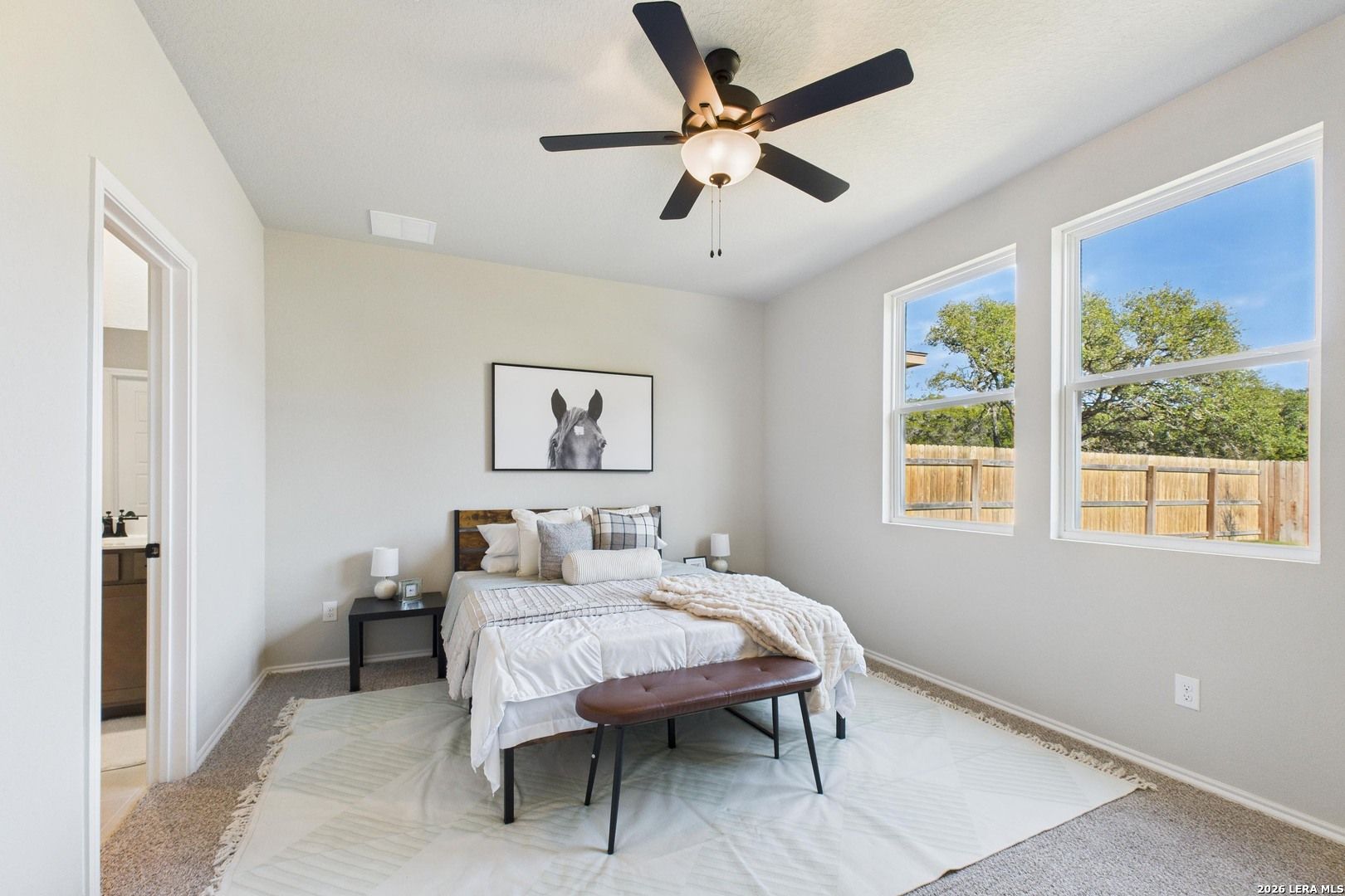 Cozy secondary bedroom with queen bed, ceiling fan, horse artwork, and backyard views in Davidson Homes The Douglas E, San Antonio