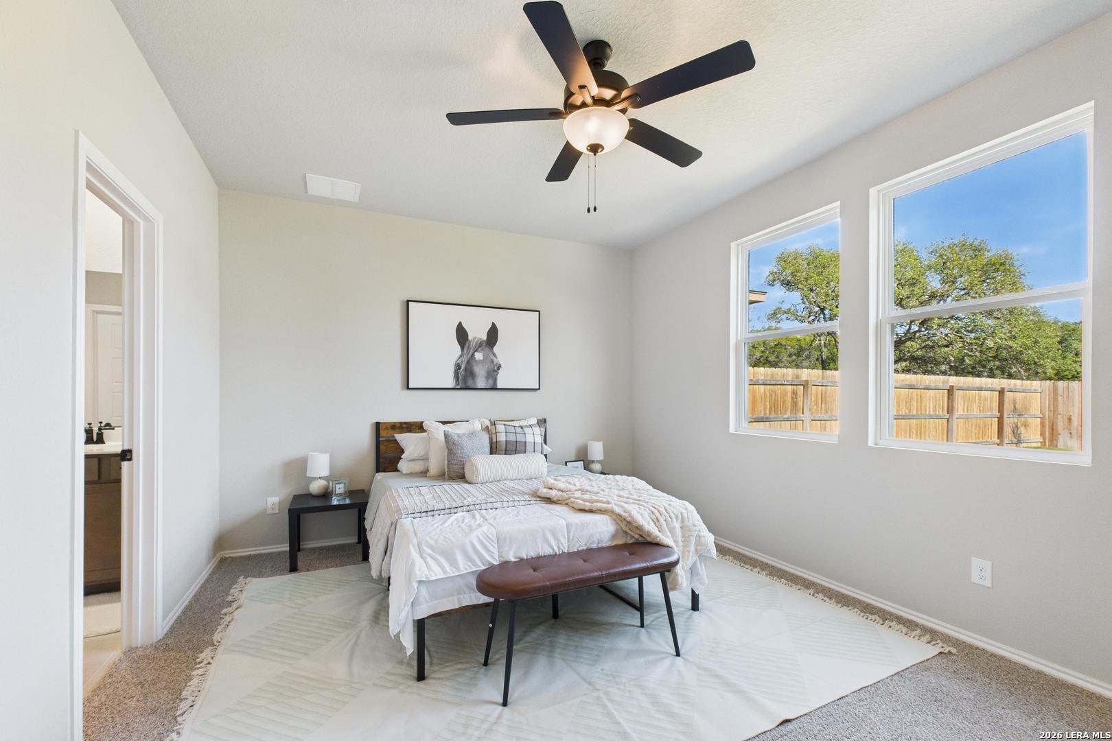 Cozy secondary bedroom with queen bed, ceiling fan, horse artwork, and backyard views in Davidson Homes The Douglas E, San Antonio