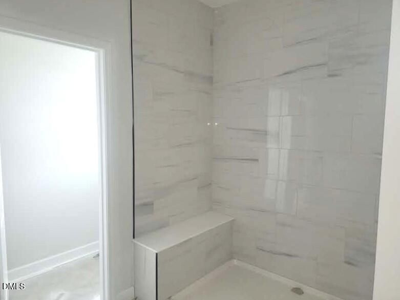 Modern walk-in shower with white marble-style tile and built-in bench in The Crawford D home in Angier, North Carolina.