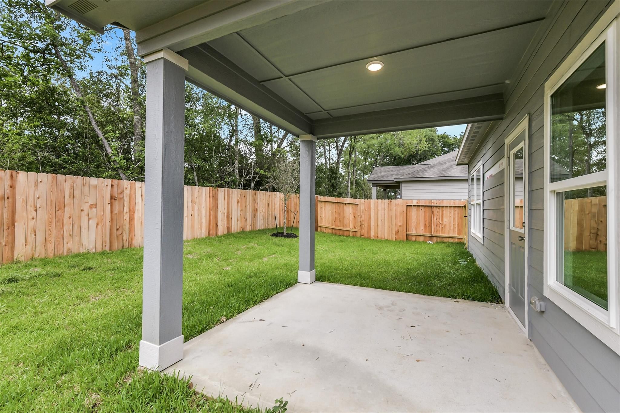 Covered back patio with concrete slab, lush green yard, and wooden privacy fence in Davidson Homes The Brazos F, Conroe Texas