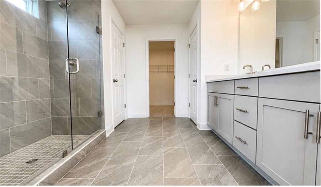 Modern primary bathroom with tile walk-in shower and dual vanity in The Hickory C floor plan at Wehunt Meadows, Hoschton.