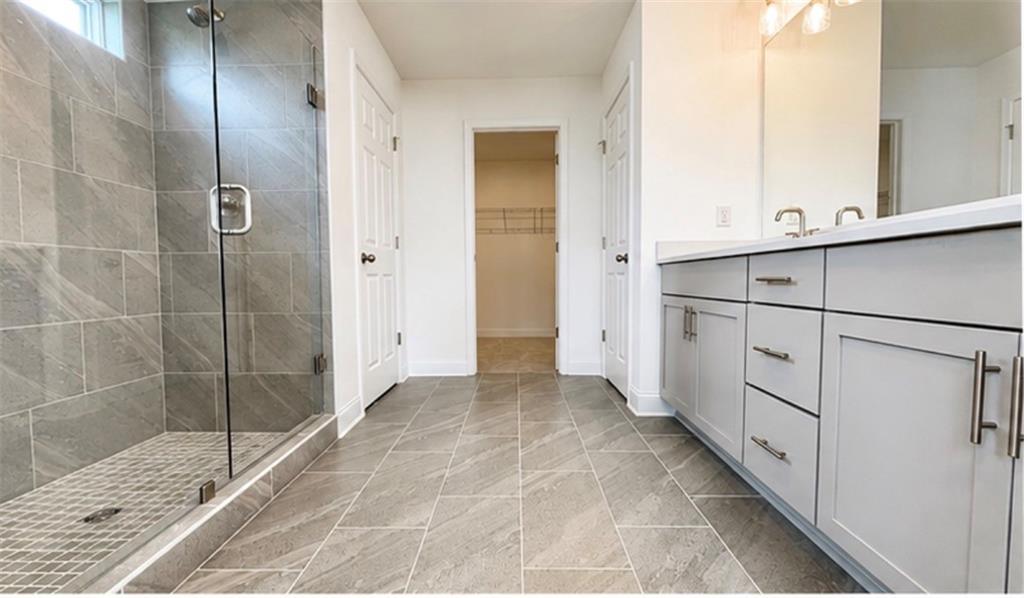 Modern primary bathroom with tile walk-in shower and dual vanity in The Hickory C floor plan at Wehunt Meadows, Hoschton.