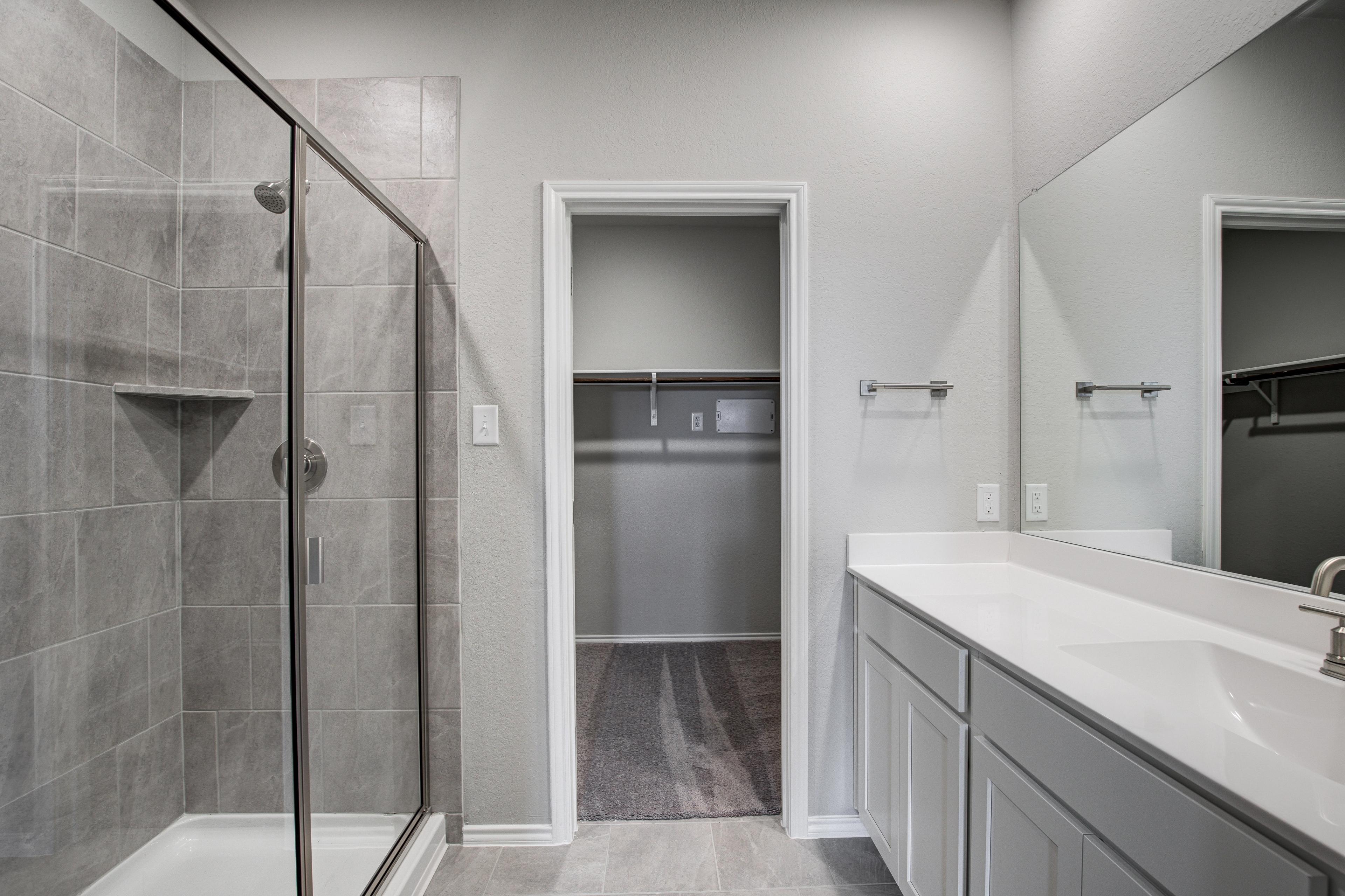 Spacious master bathroom in The Blanco C featuring frameless glass walk-in shower, gray subway tile, double white vanity, and closet door