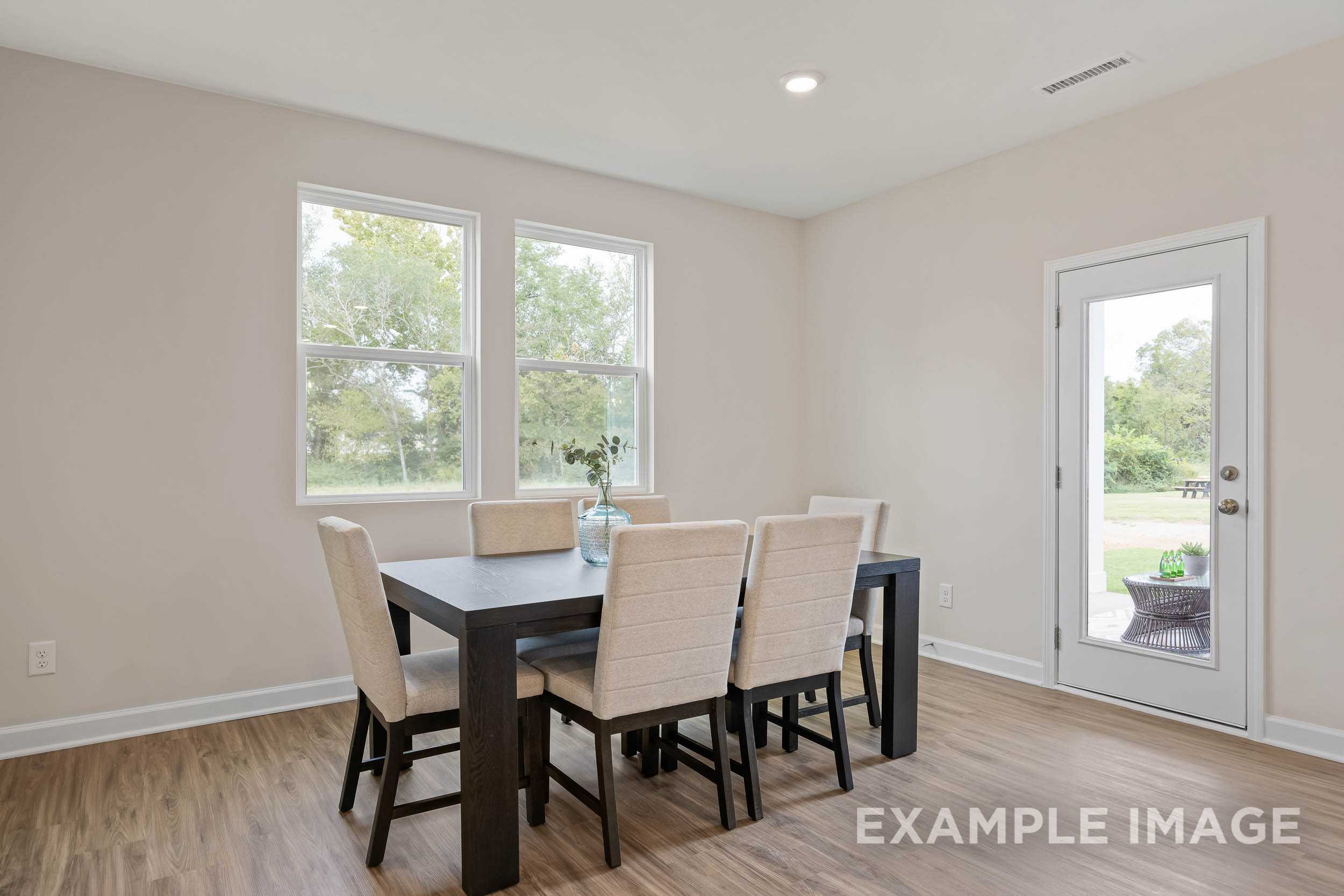 Spacious dining room in The Preston B with wooden table, beige chairs, large windows, French doors to patio, hardwood floors