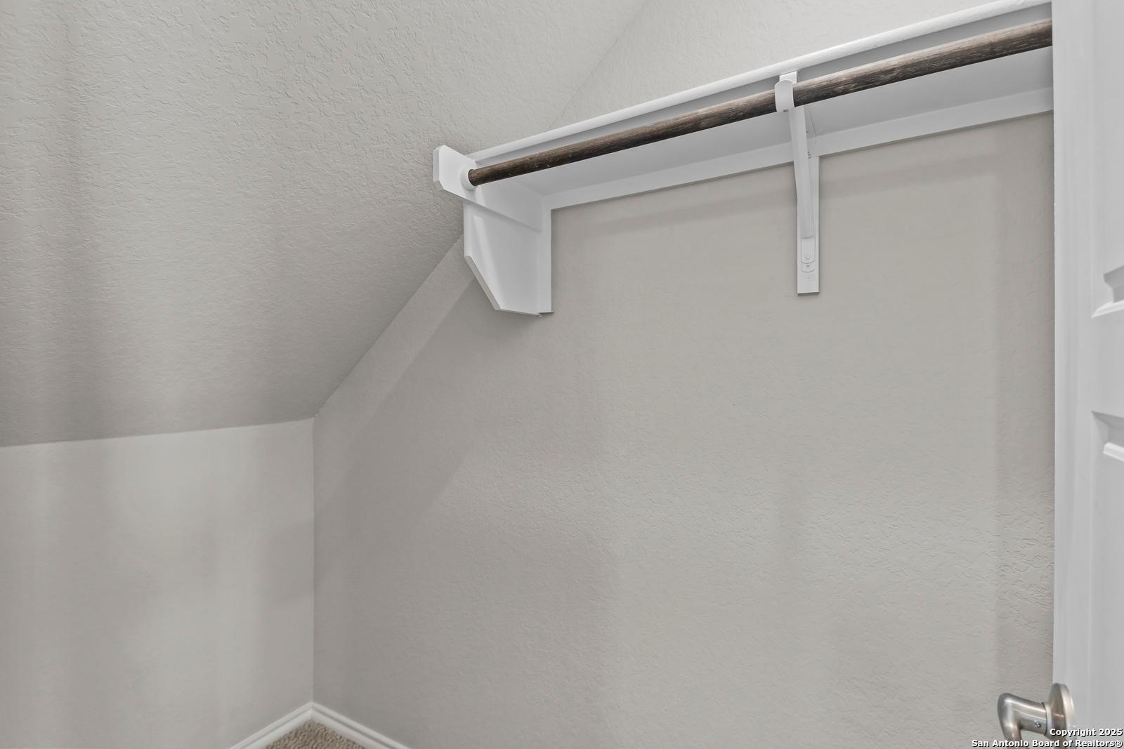 Spacious walk-in closet with mounted hanging rod and white brackets in The Collin B master suite, Seguin Texas