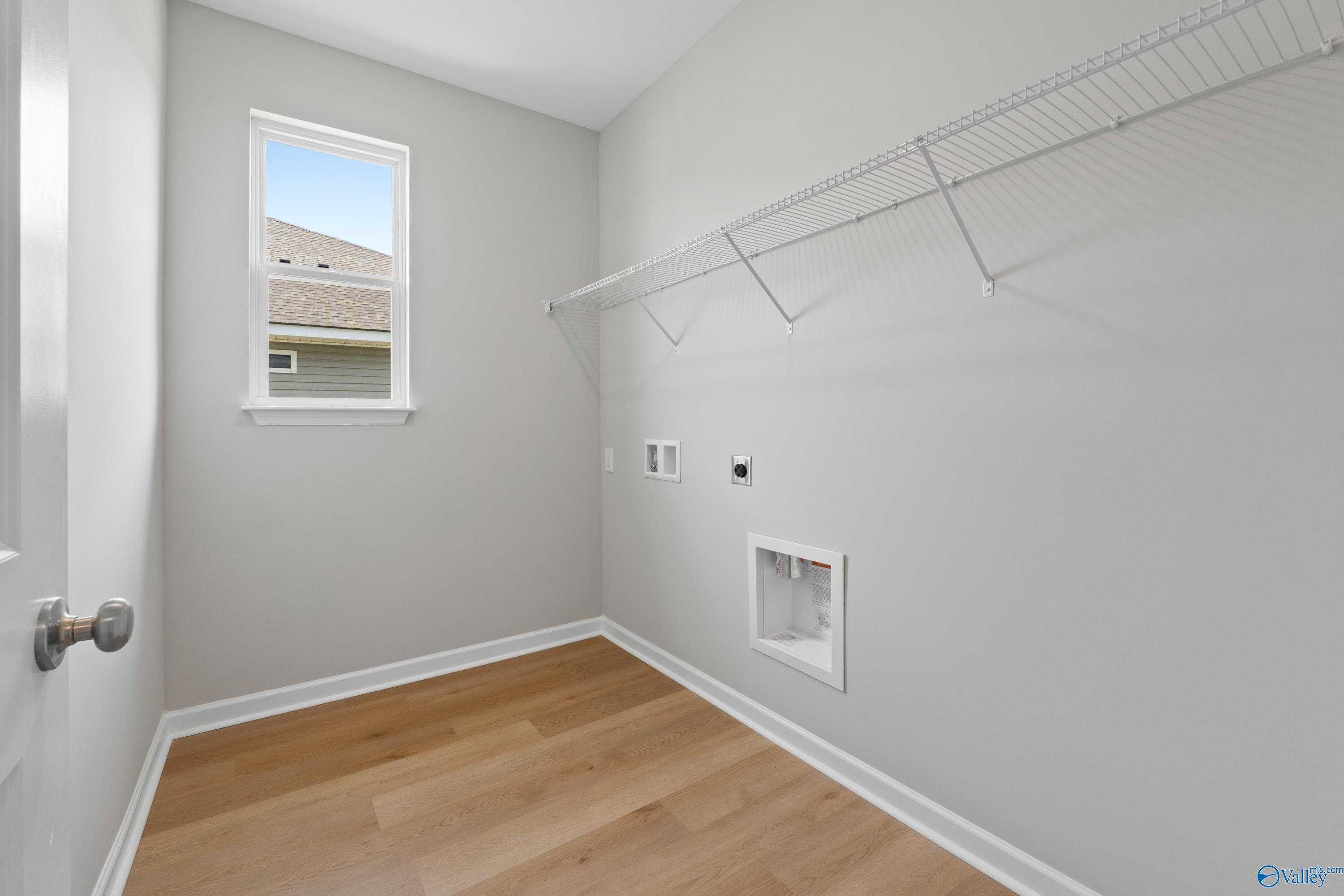 Bright laundry room with gray walls, wire shelving, washer dryer hookups, and hardwood floors in Evermore Homes The Aurora, Harvest AL