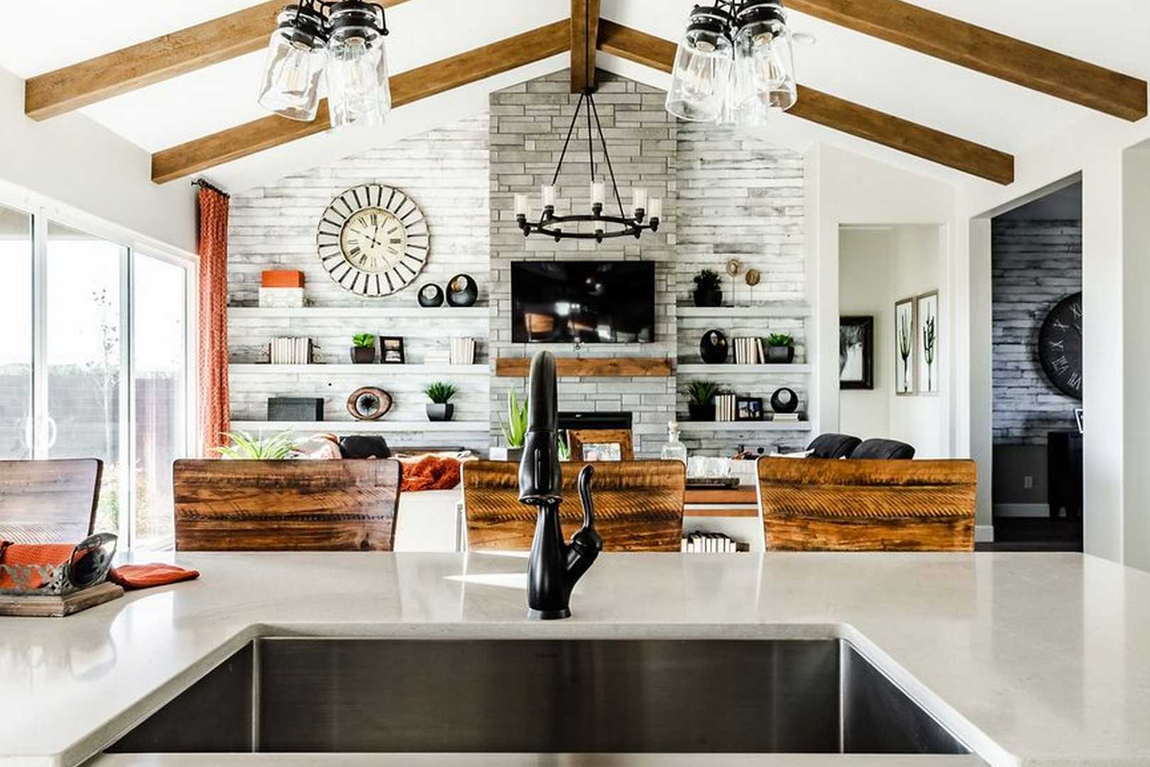 Open-concept kitchen and living area in The Monarch home with white quartz counters, stone fireplace, wooden beams, and chandelier