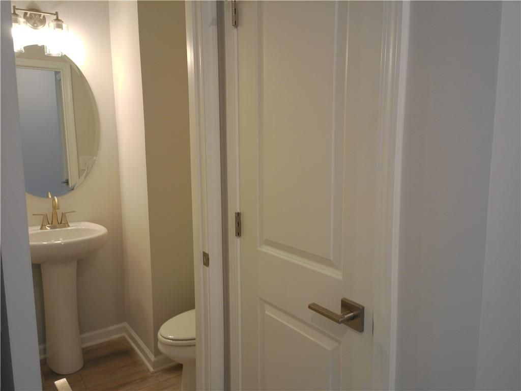 Elegant powder room with pedestal sink, round mirror, and white toilet in Davidson Homes The Marion C, Winder, Georgia