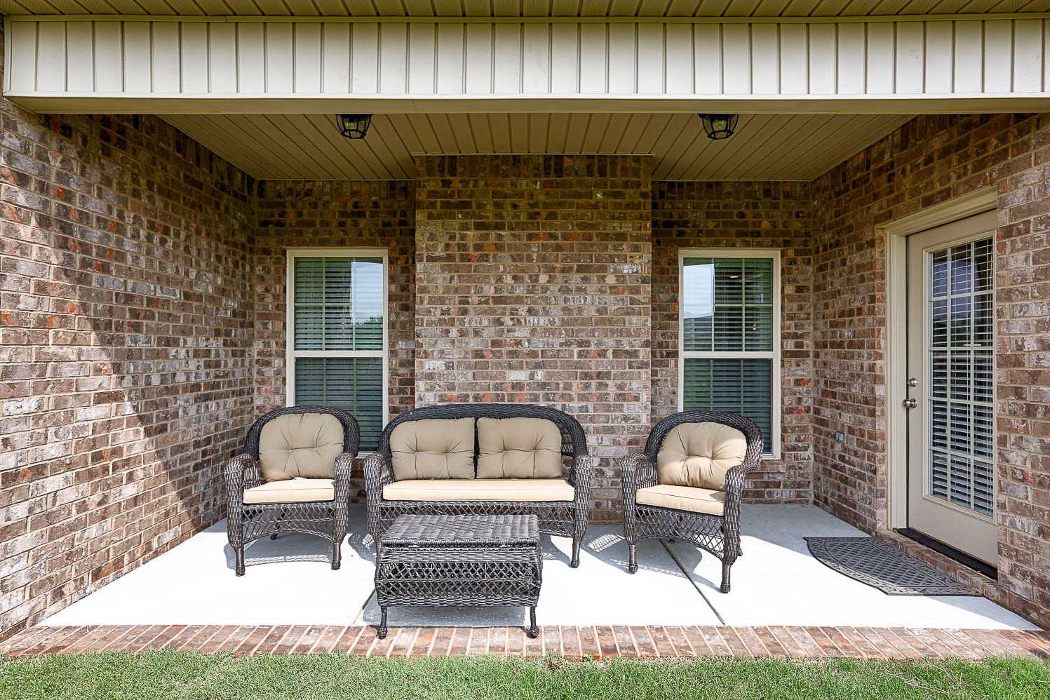 Spacious covered patio of The Finleigh with brick walls, large windows, French door, and wicker outdoor seating on concrete floor