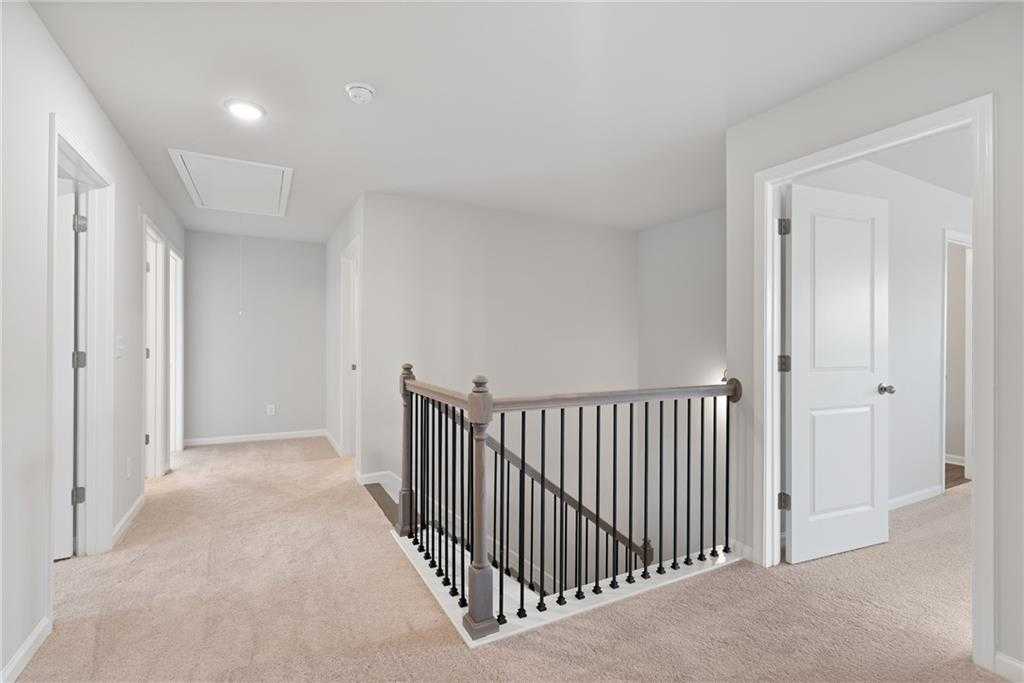 Spacious second-floor hallway with beige carpet, white walls, and wooden balustrade in Davidson Homes The Hickory B, Winder, GA