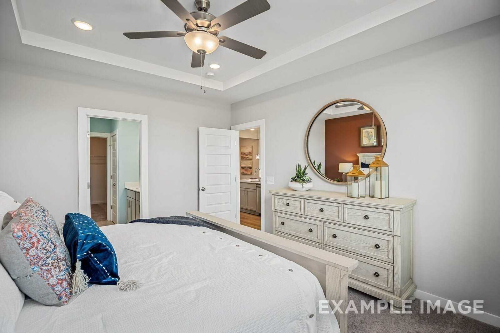 Elegant master bedroom with ceiling fan, king bed, gold round mirror, white dresser, and en-suite bath in Davidson Homes The Franklin B, White House, Tennessee
