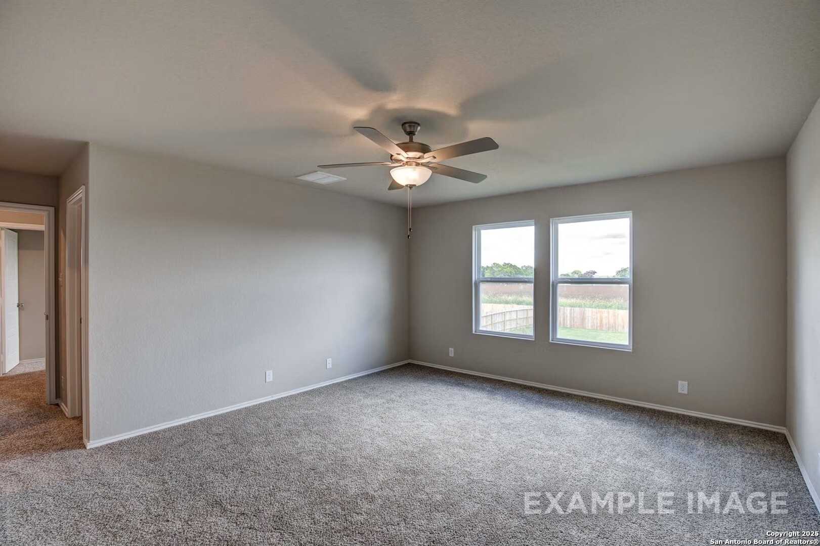 Spacious carpeted bedroom with ceiling fan, large windows overlooking fenced backyard in Davidson Homes The Murray K, San Antonio