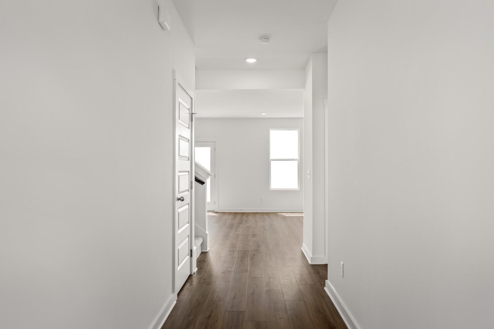 Bright hallway with modern wood-look flooring and white paneled door in The Henry C floor plan at Calista Farms.