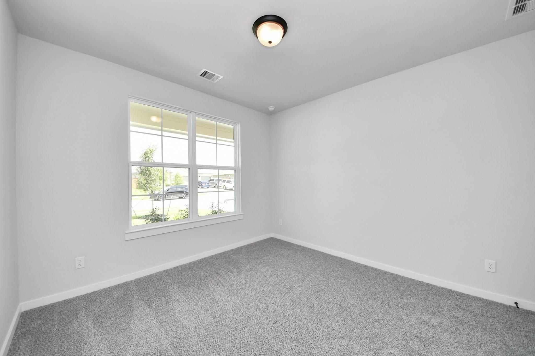 Bright, carpeted bedroom with large window in The Everett C floor plan at River Ranch Meadows, Dayton, Texas.