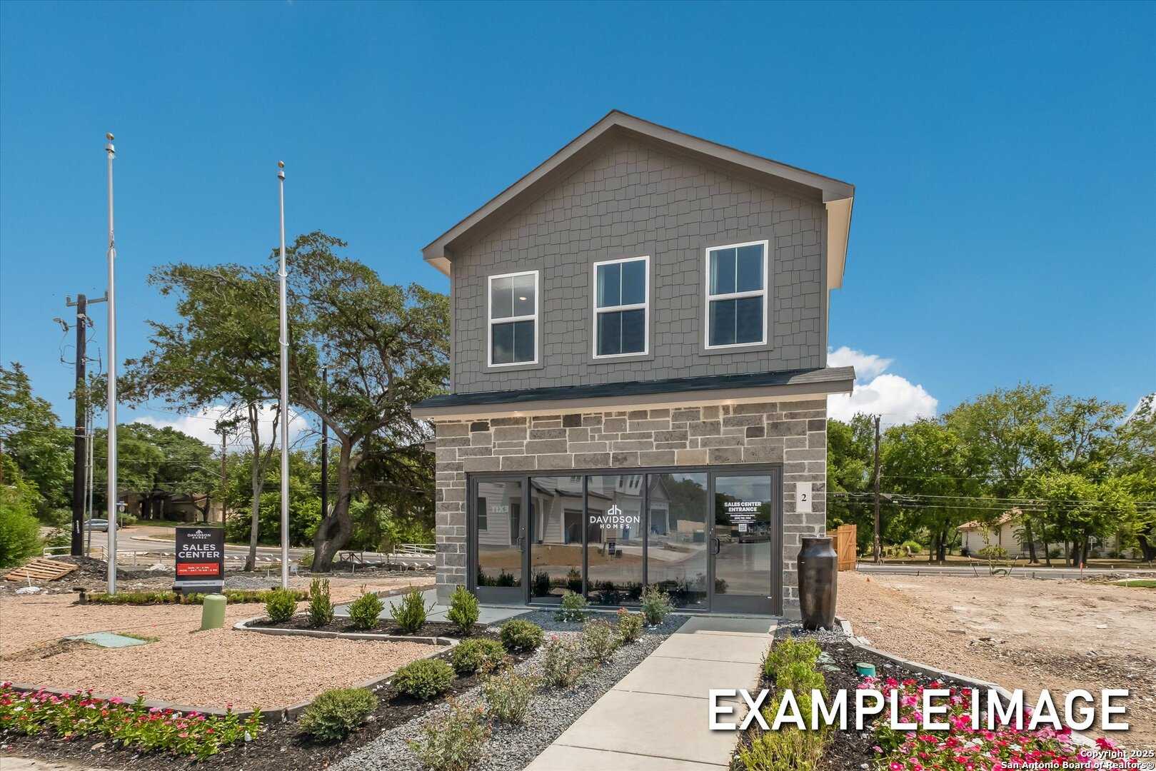 Modern two-story gray home exterior with stone accents, large windows, and for-sale sign in Meadows at Oak Creek, San Antonio, Texas