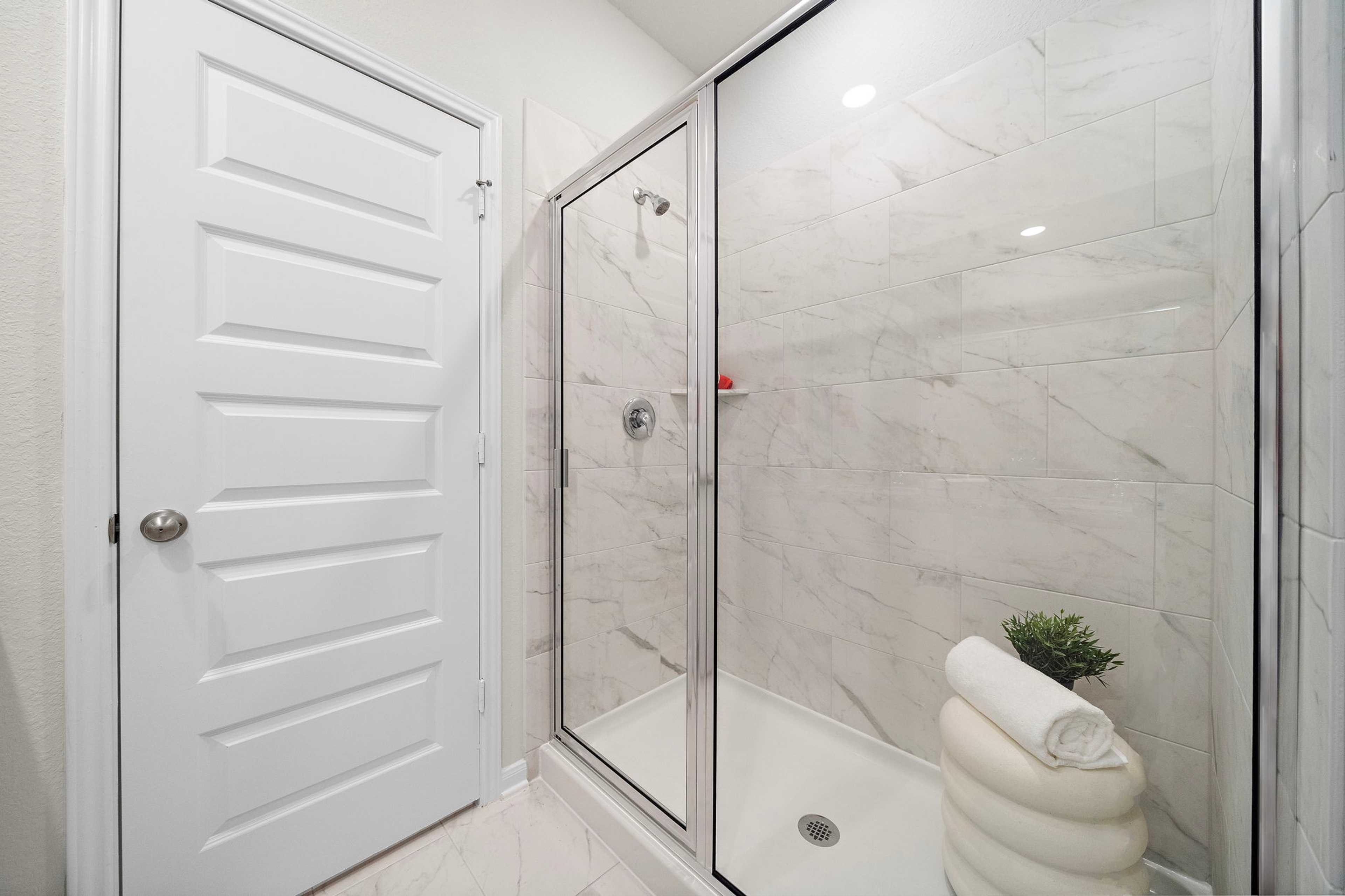 Modern bathroom with glass shower at Liberty Estates in Cleveland Texas featuring white subway tiles potted plant and rolled towels